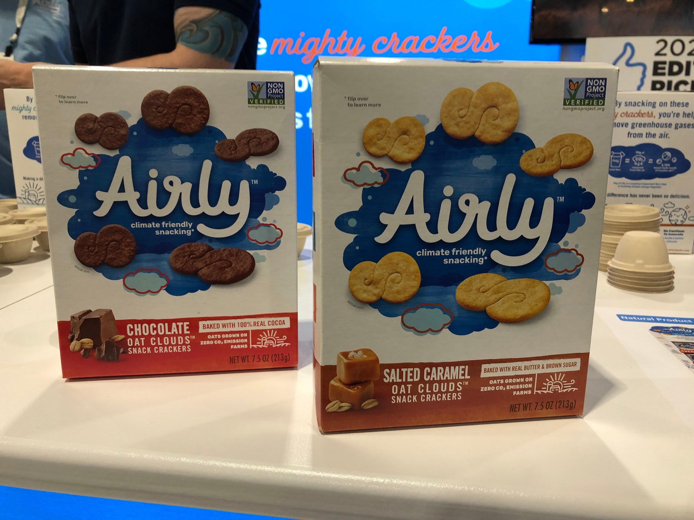 Boxes of Airly chocolate and salted caramel oat clouds snack crackers on a white counter in front of a blue backdrop
