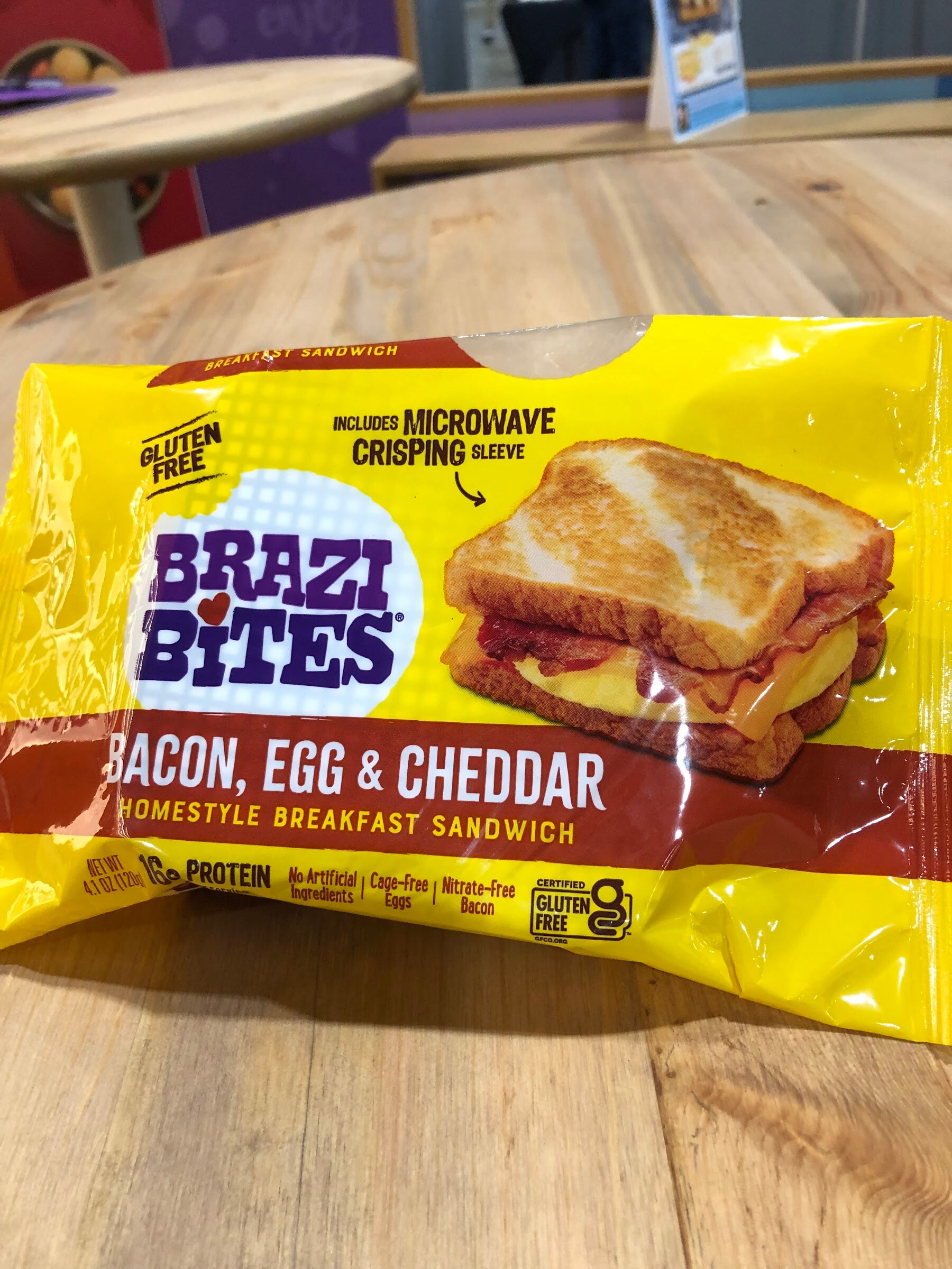 A yellow Brazi Bites bacon, egg and cheddar breakfast sandwich package on a wooden table