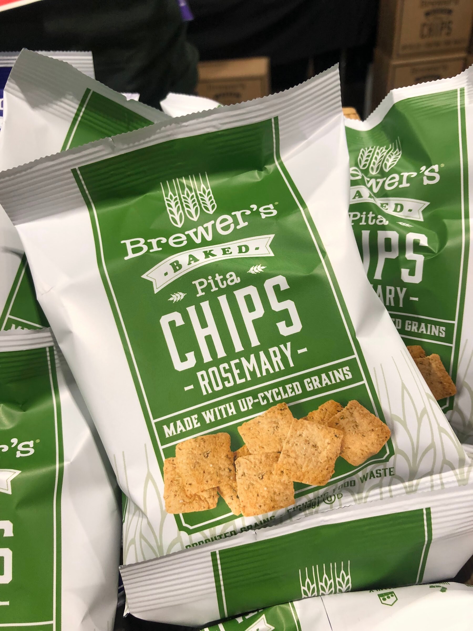 Bags of Brewer's Baked Pita Chips in rosemary, made with up-cycled grains, in green and white packaging