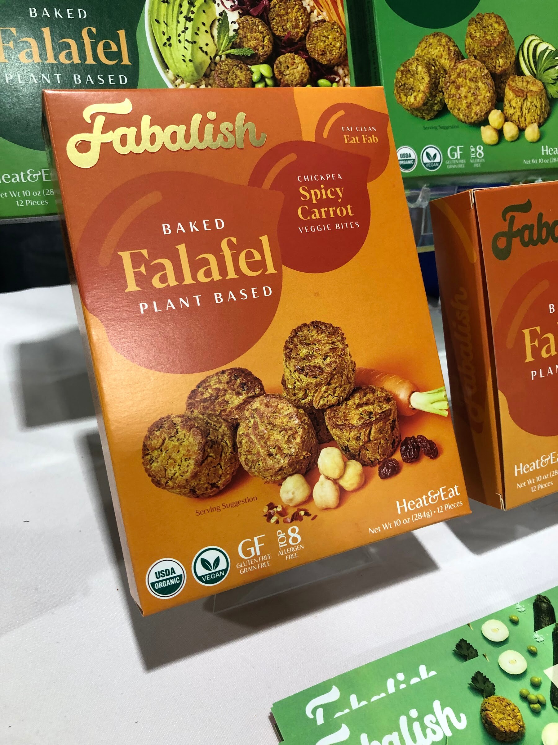 Fabalish baked spicy carrot falafel boxes on a white table in front of a green display