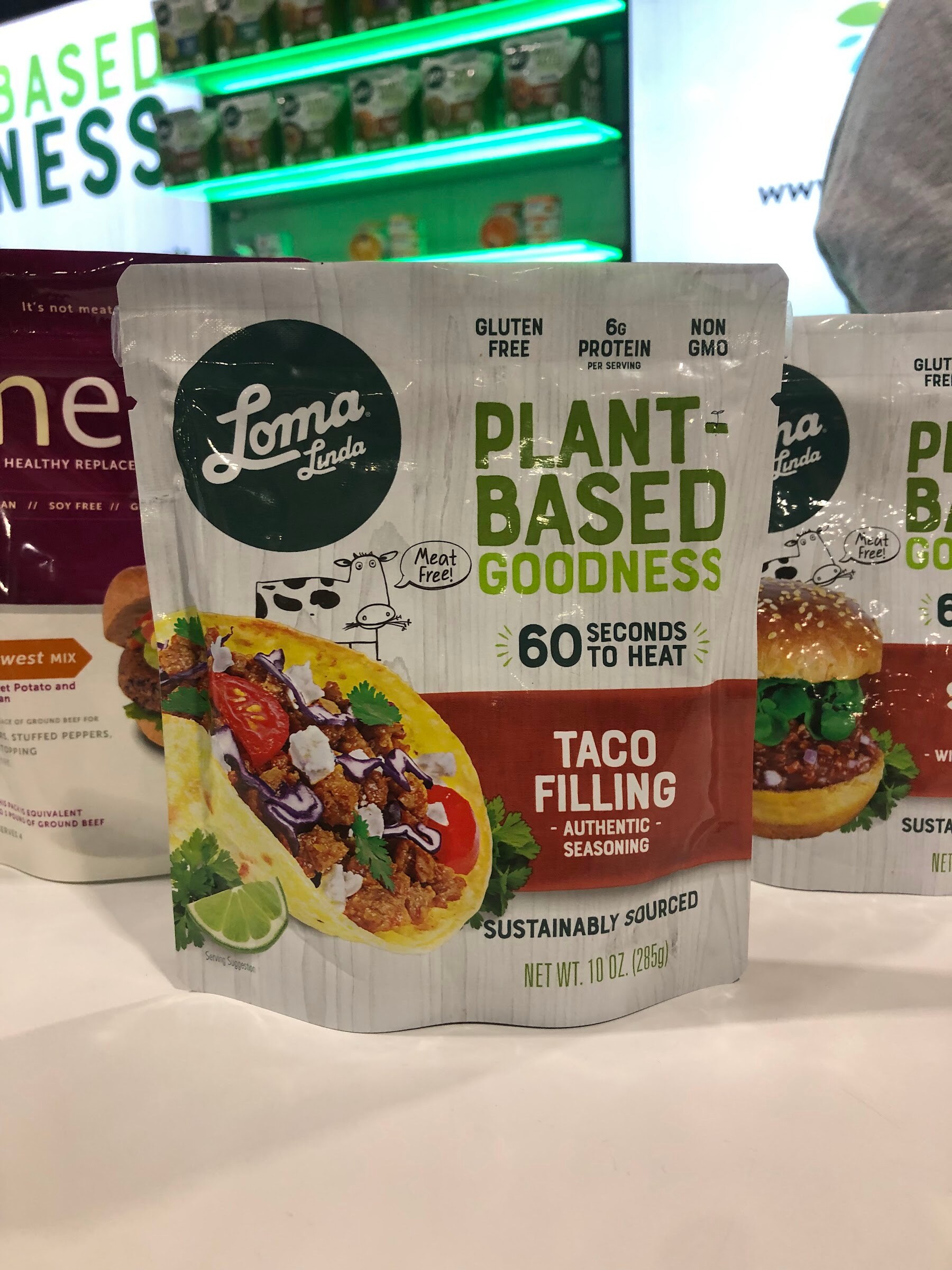 A Loma Linda Plant-Based Goodness taco filling pouch stands on a white counter beside other Loma Linda packages