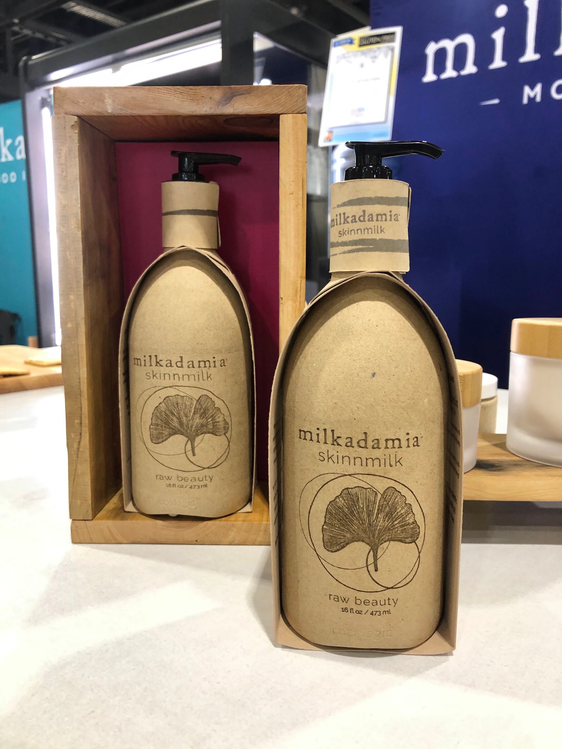 Two kraft-colored milkadamia skinnmilk pump bottles, one in a wooden box, on a white counter