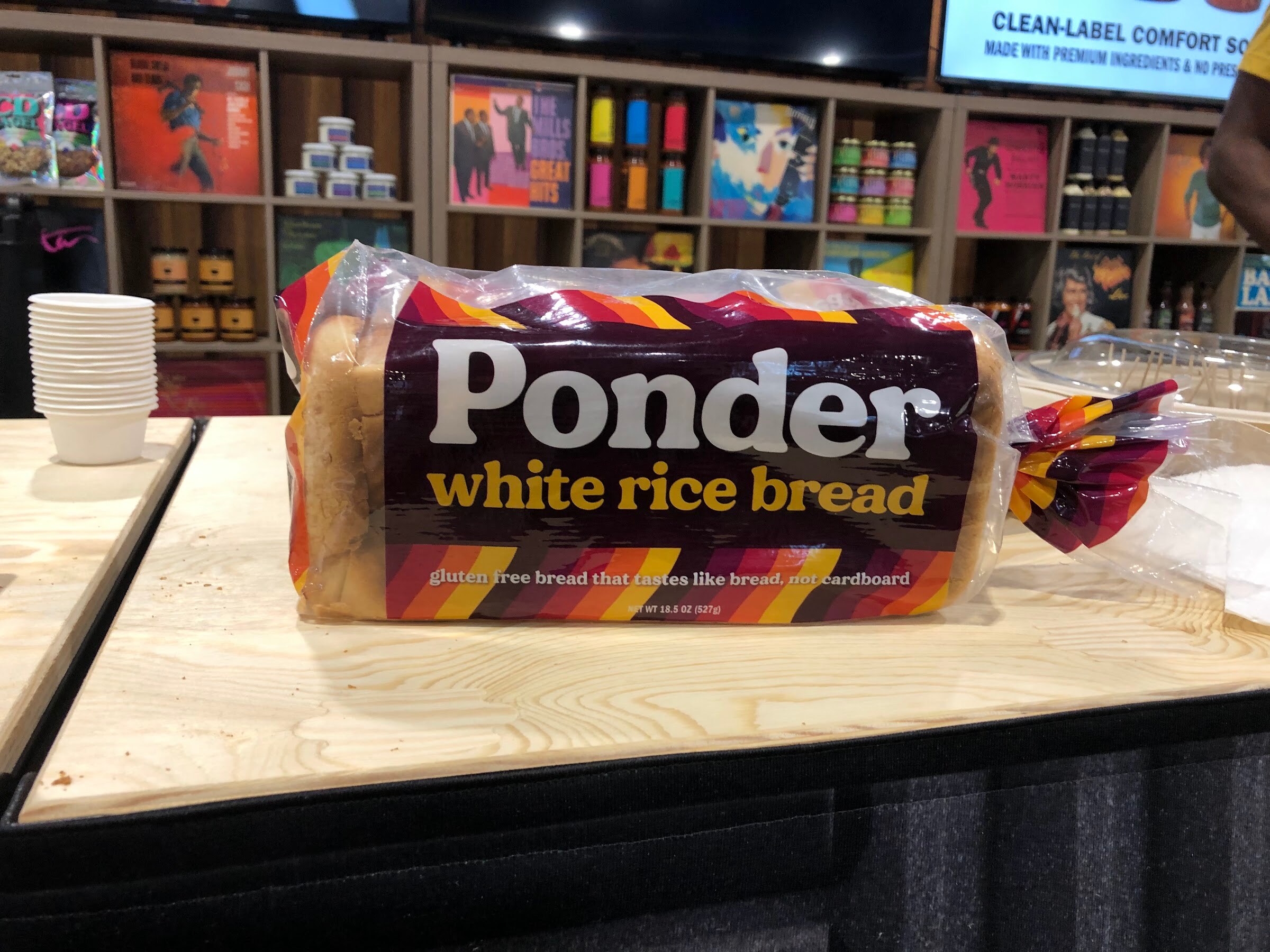 A loaf of Ponder white rice bread on a wooden counter in front of shelves of colorful products