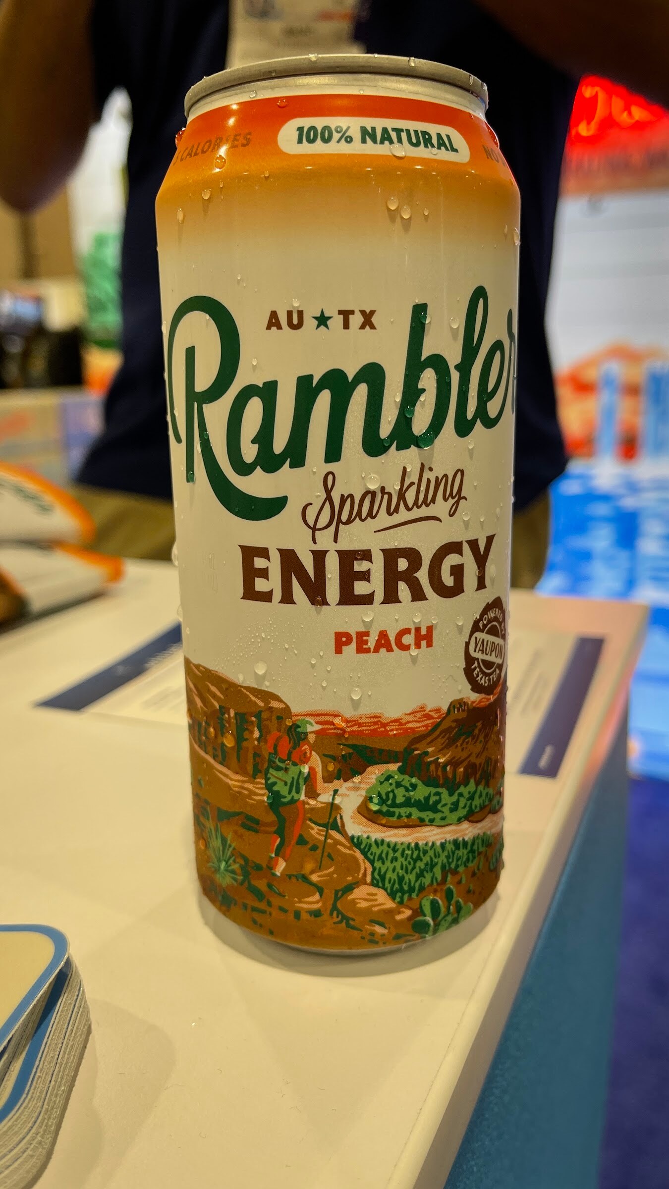 A Rambler peach sparkling energy can on a table with a colorful backdrop