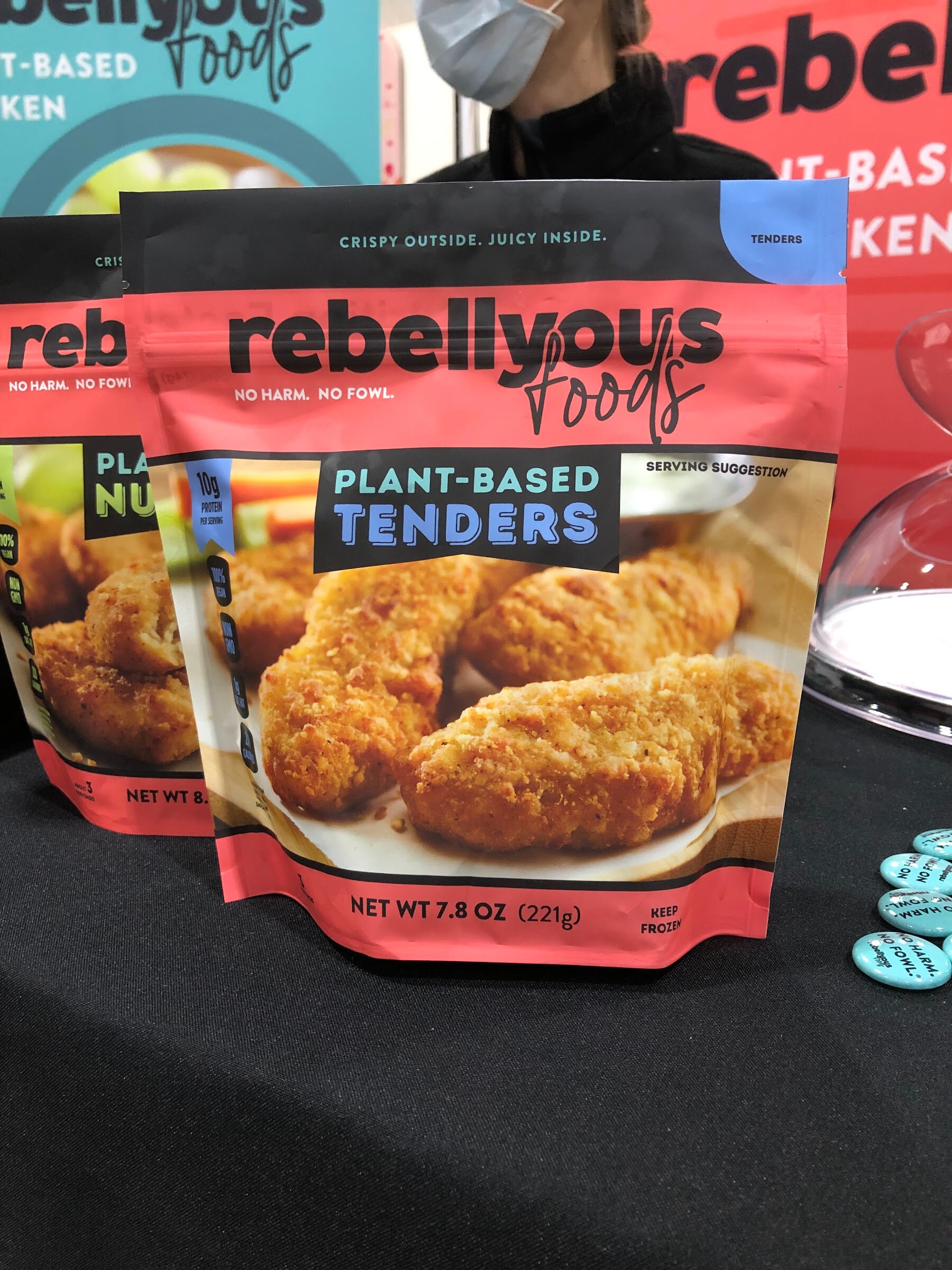 A Rebellyous Foods plant-based tenders bag on a black tablecloth with other Rebellyous packages behind
