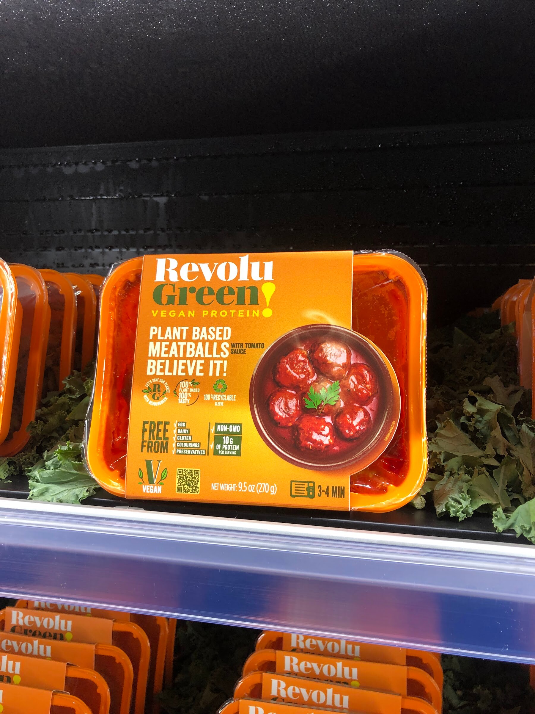 A Revolu Green plant-based meatballs package on a refrigerated shelf in front of more packages