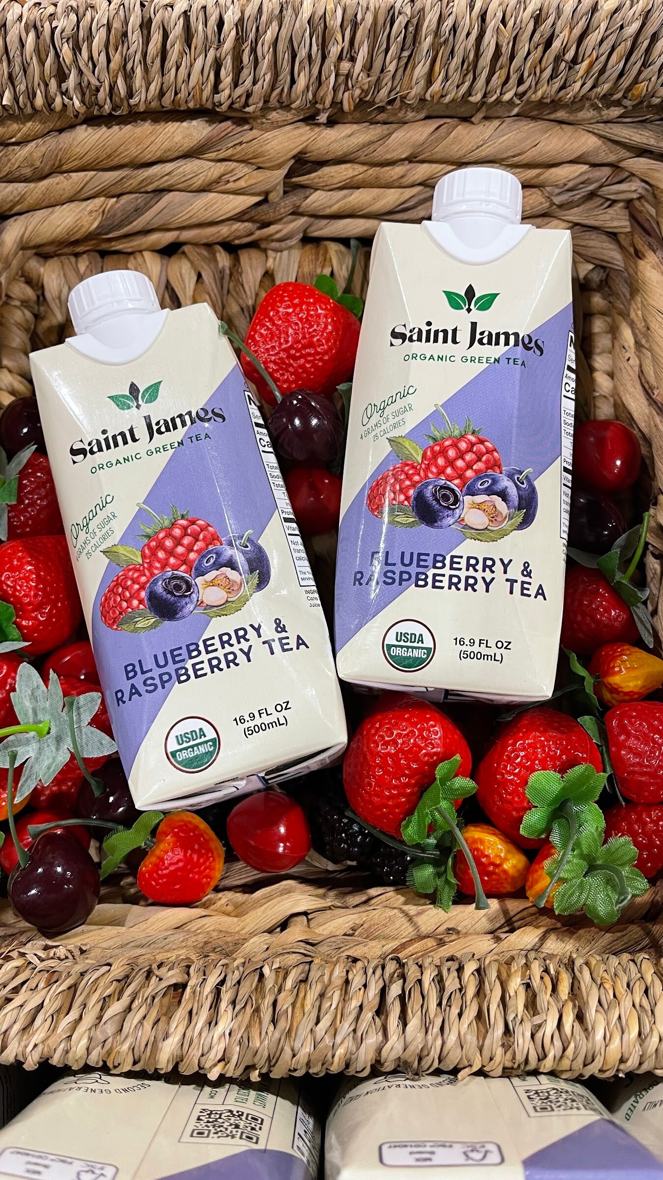 Two Saint James blueberry and raspberry tea cartons in a woven basket surrounded by strawberries