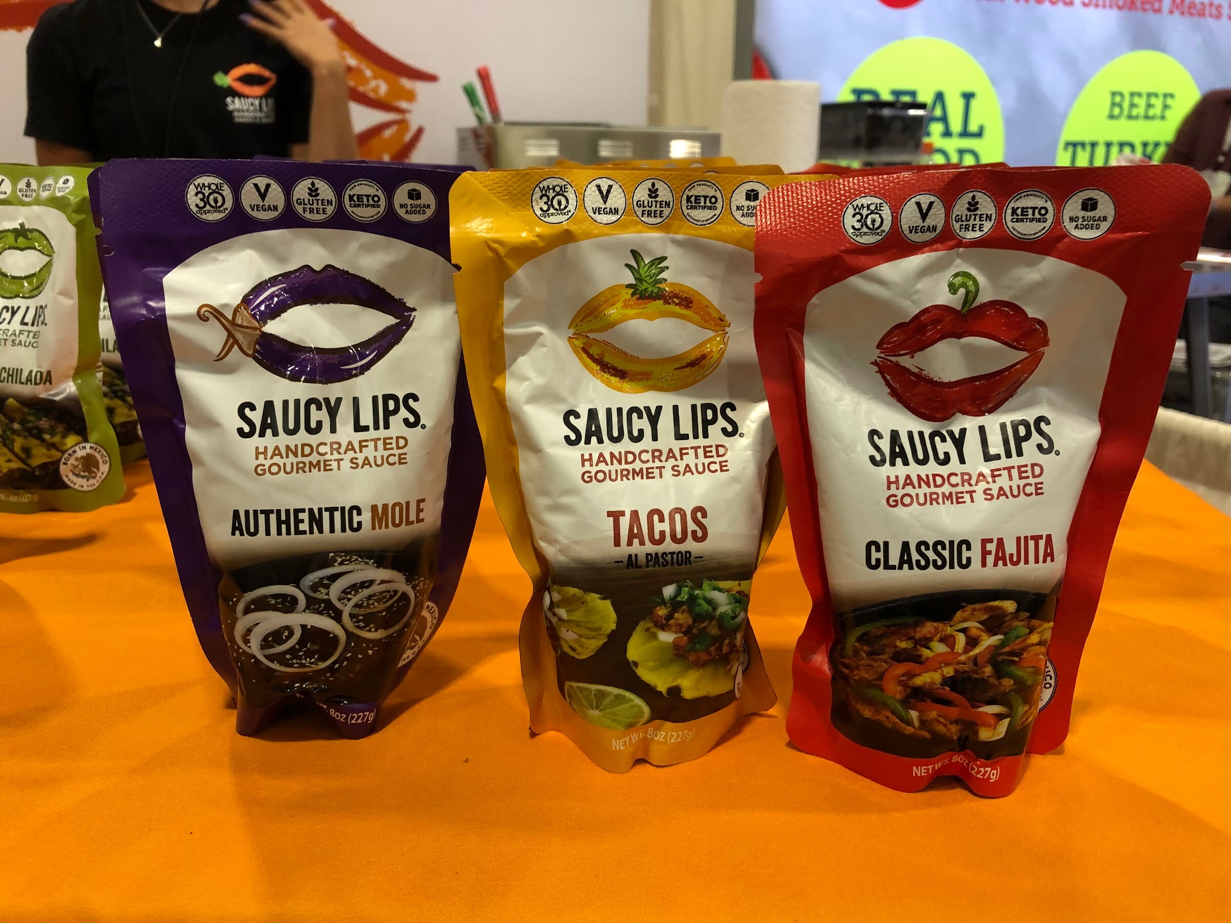 Three Saucy Lips sauce pouches, Authentic Mole, Tacos and Classic Fajita, on an orange tablecloth