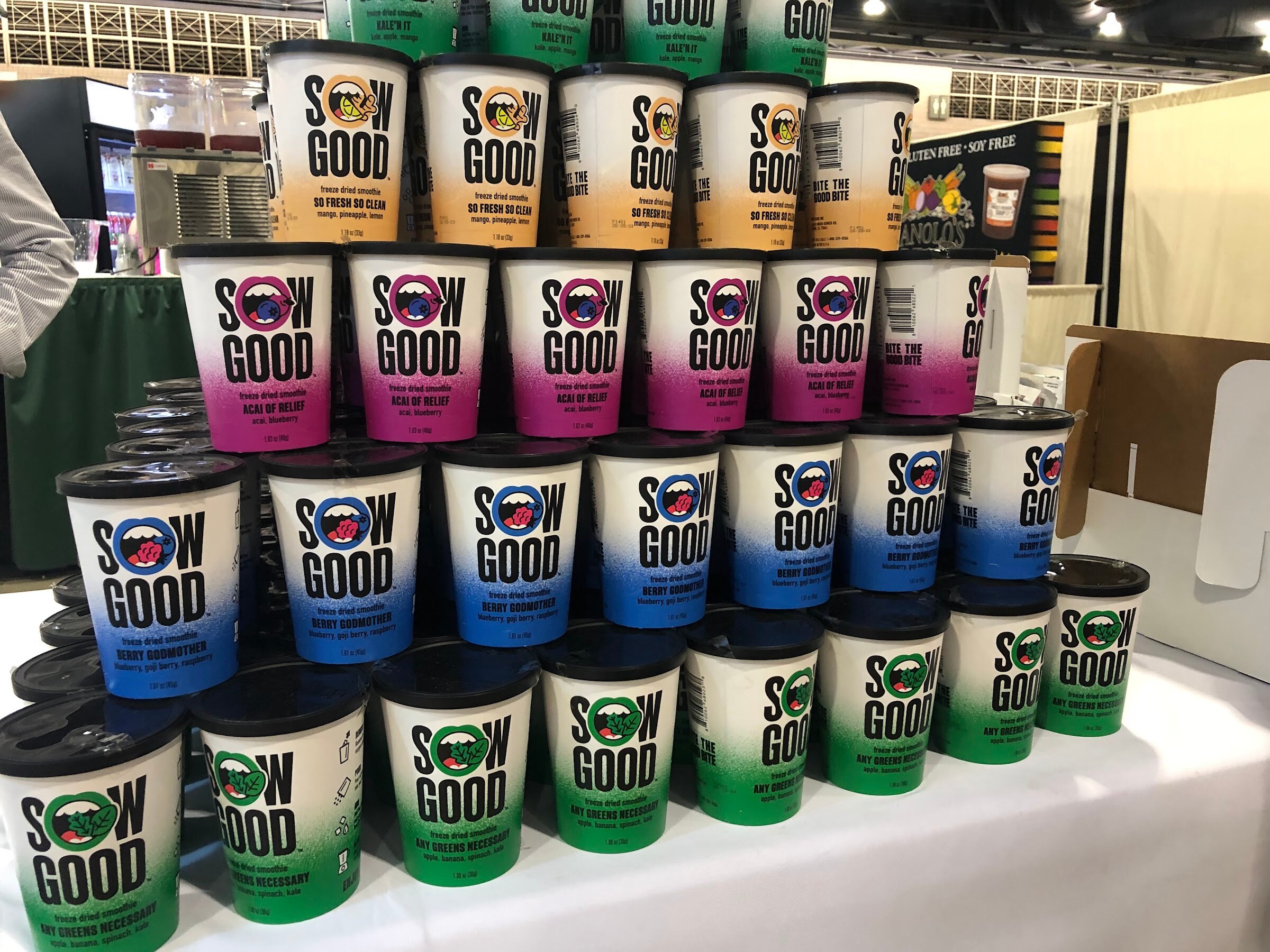 A tall pyramid of Sow Good cups in orange, pink, blue and green gradients on a booth table