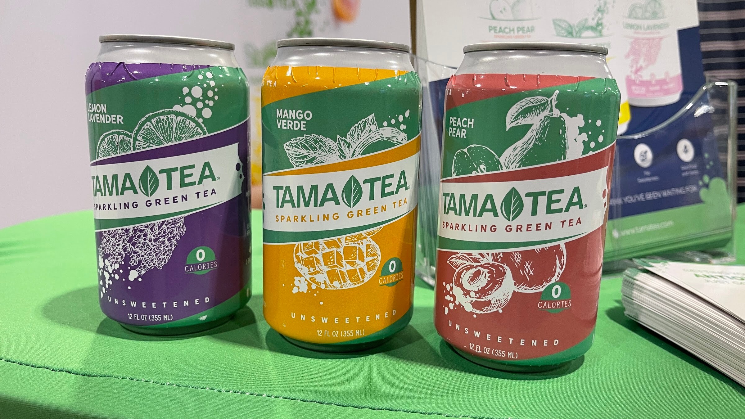 Three TAMA TEA sparkling green tea cans in lemon lavender, mango verde and peach pear on a green table