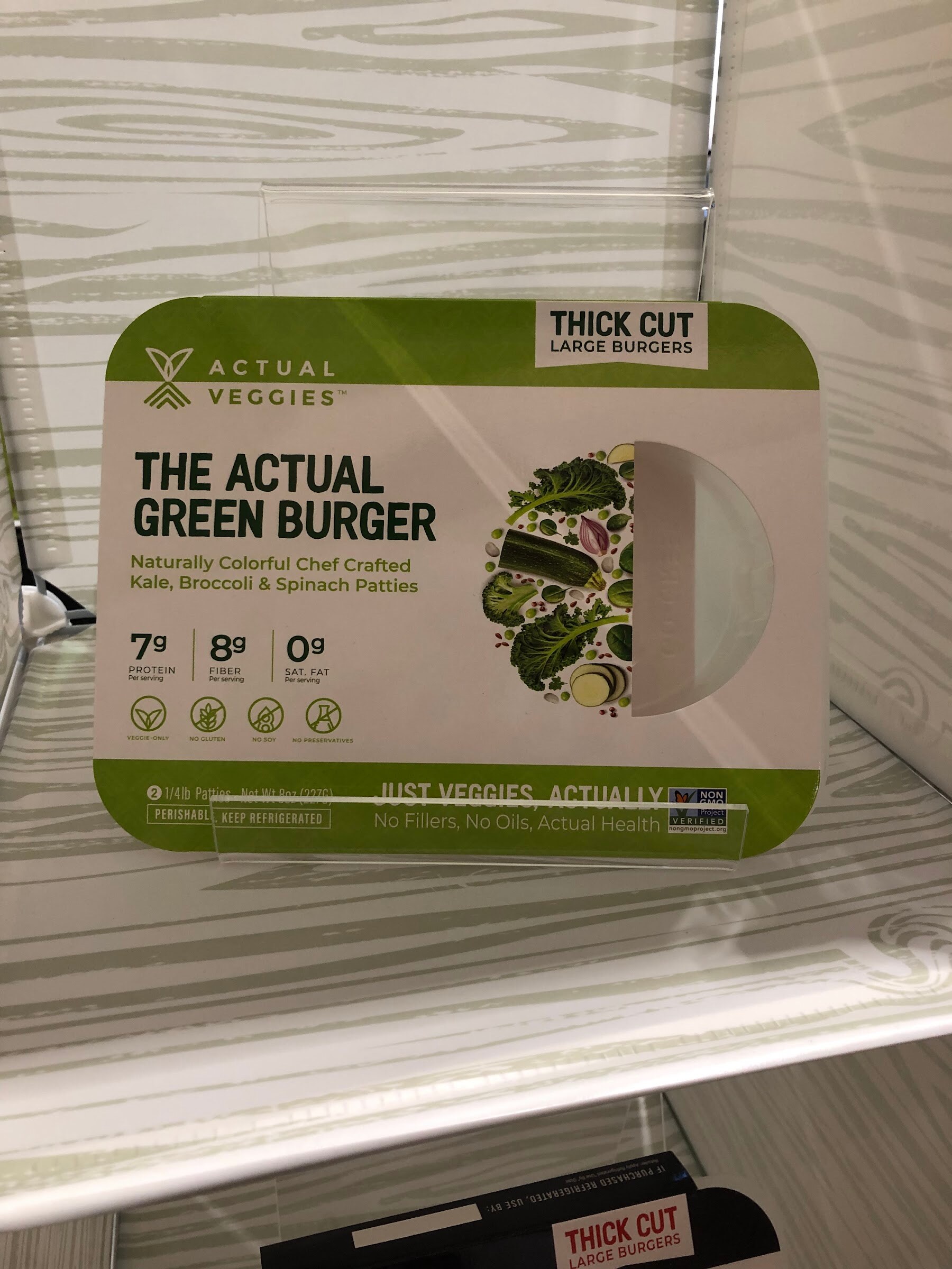 A package of The Actual Veggies green burger with kale, broccoli and spinach on a white wood-grain shelf