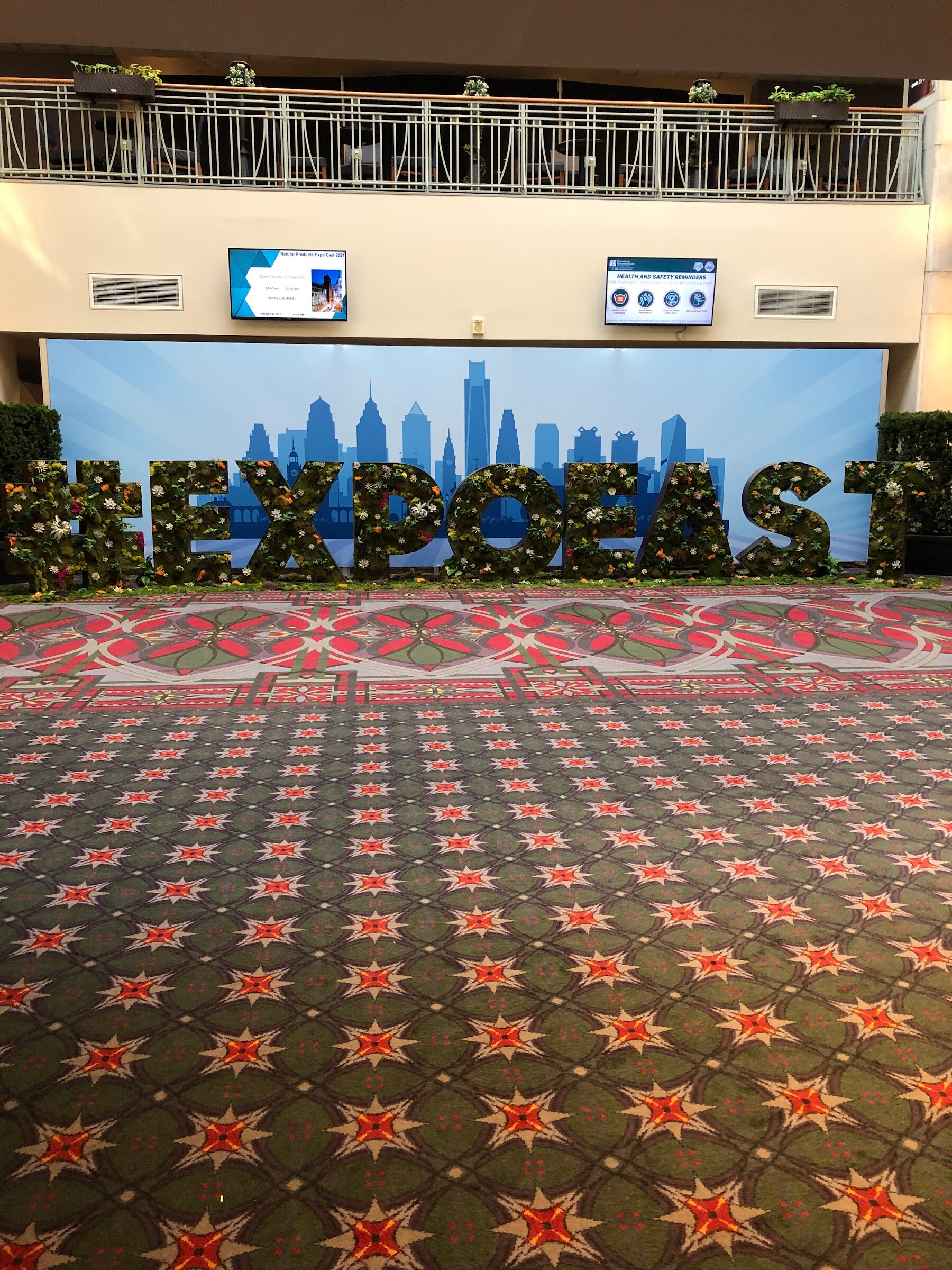 Large topiary letters spelling EXPO EAST in front of a blue Philadelphia skyline backdrop on a patterned carpet