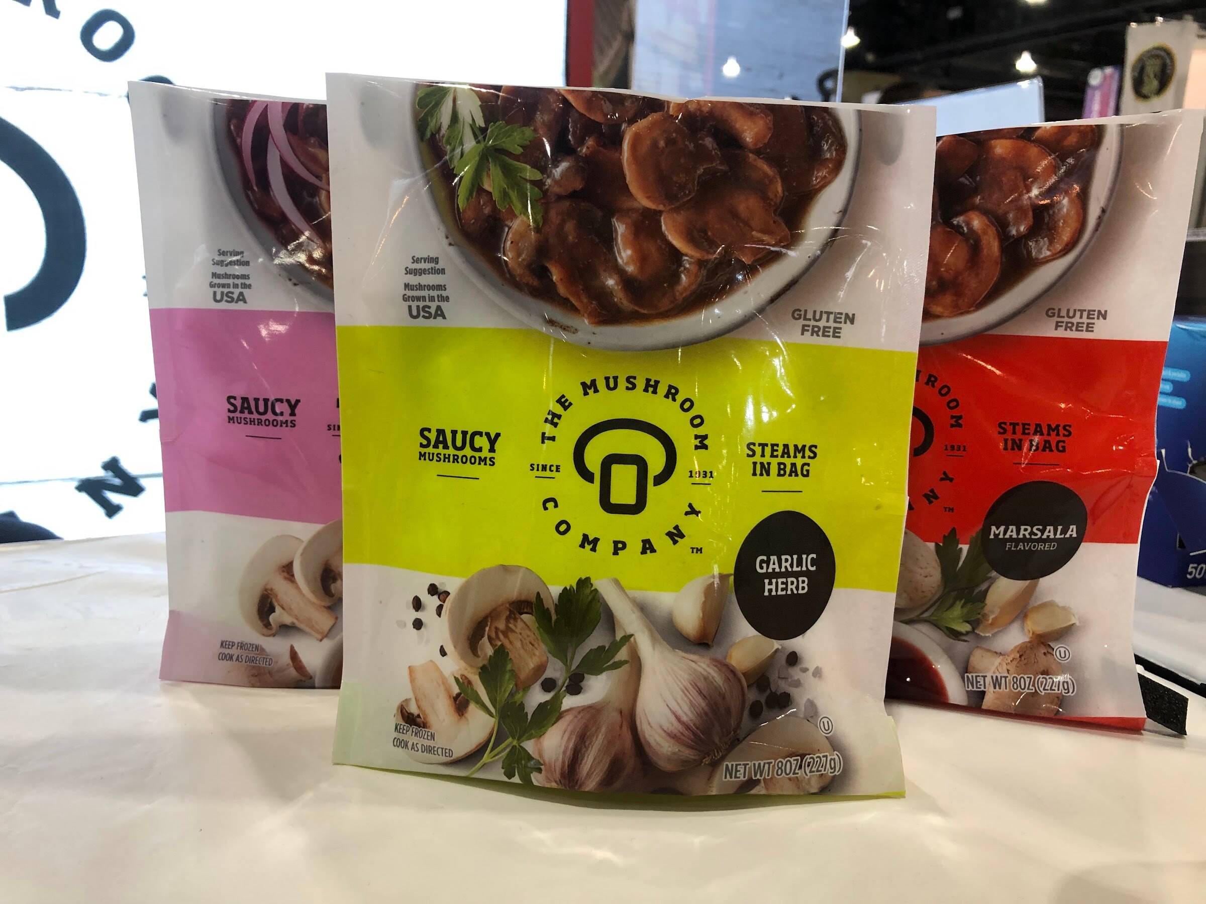 Packages of The Mushroom Company saucy mushrooms in garlic herb and other flavors on a white counter