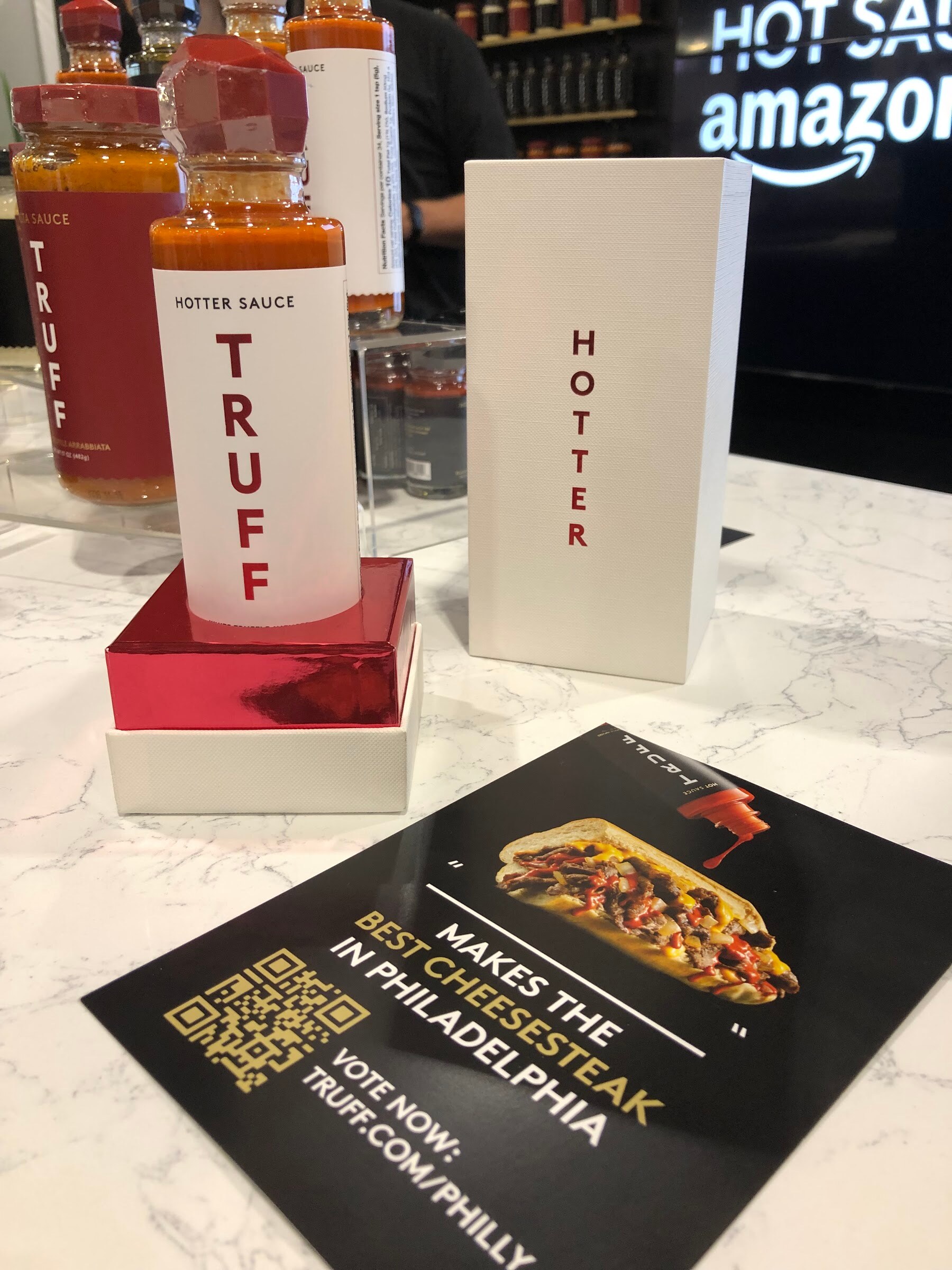 A bottle of TRUFF hotter sauce on a red riser beside a card about the best cheesesteak in Philadelphia