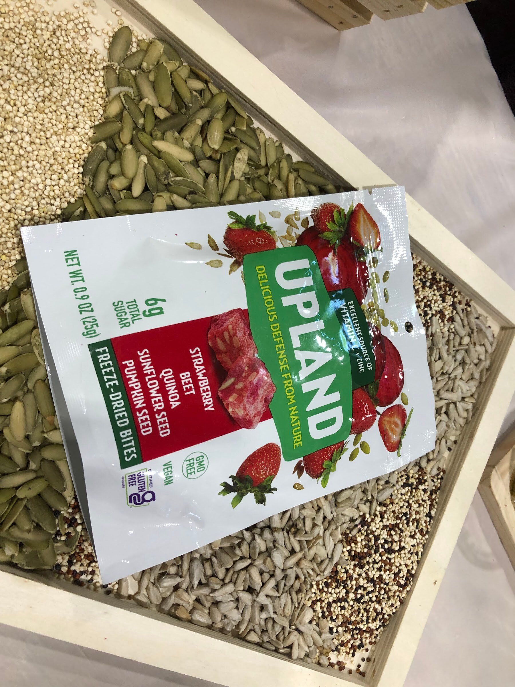 A bag of Upland strawberry beet freeze-dried bites on a wooden tray filled with seeds and quinoa