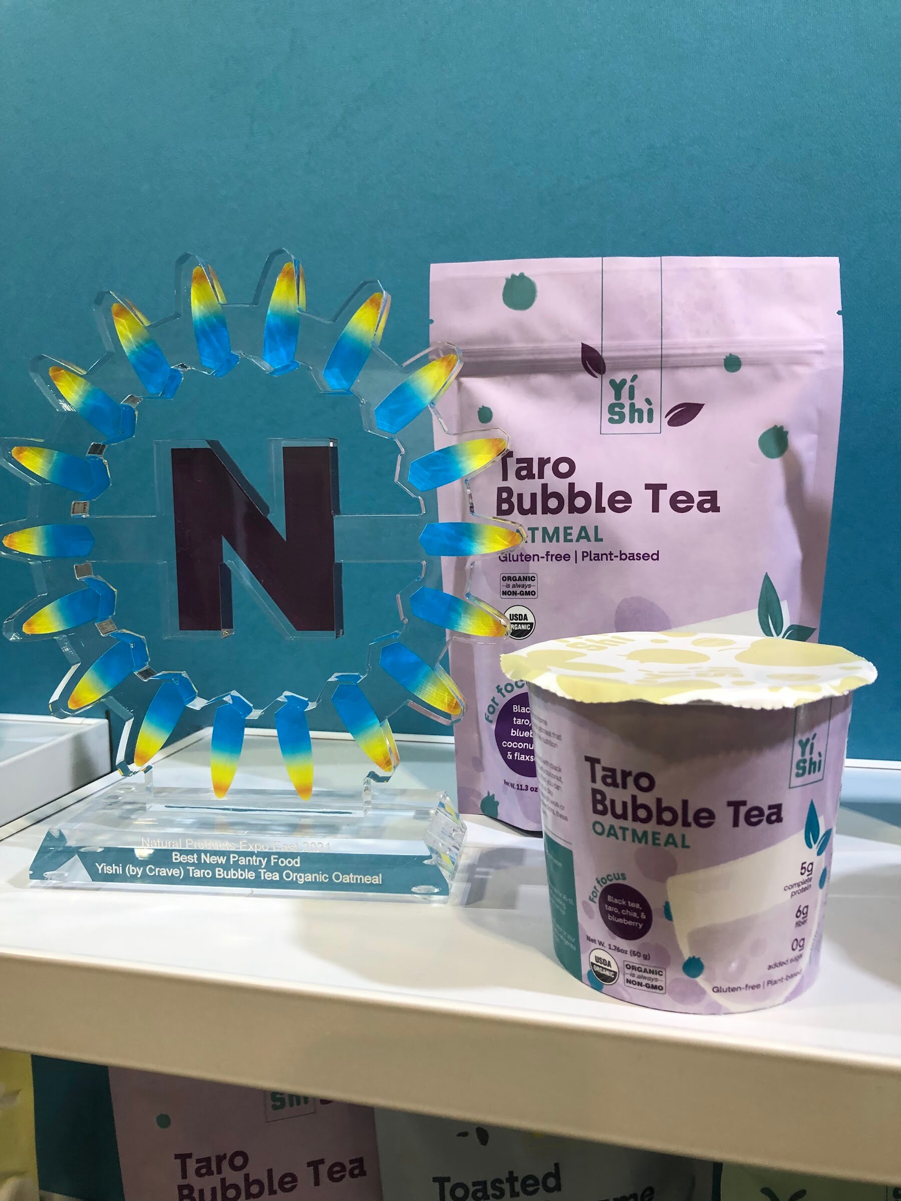 A Yishi Taro Bubble Tea oatmeal pouch and cup beside a blue and yellow Nexty award trophy