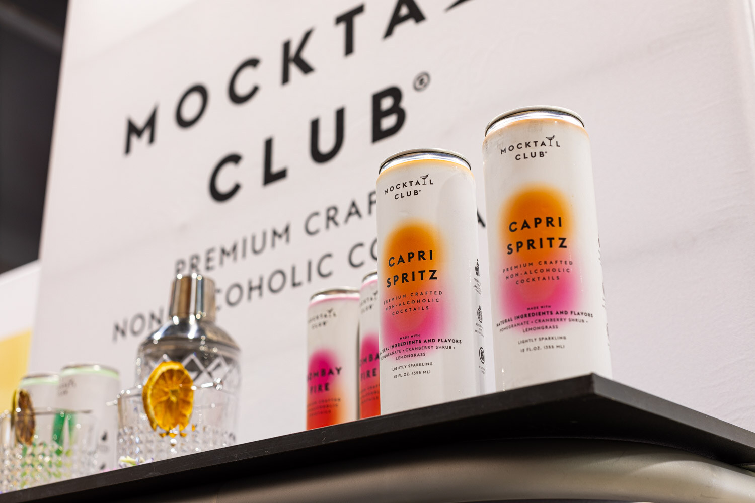 Two Mocktail Club Capri Spritz cans stand on a shelf beneath a large Mocktail Club sign