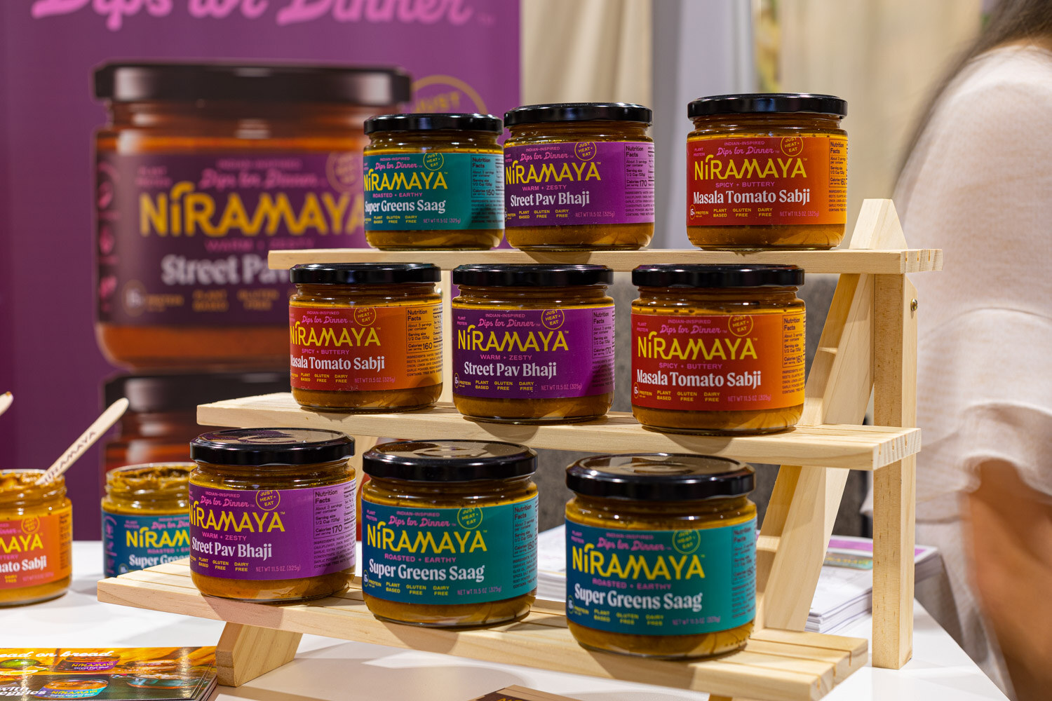 Jars of Niramaya Street Pav Bhaji, Masala Tomato Sabji and Super Greens Saag sauces are stacked on tiered wooden shelves