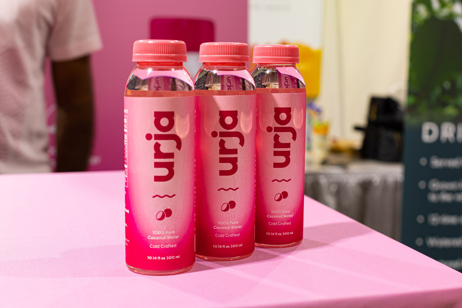 Three pink Urja bottles stand in a row on a pink table