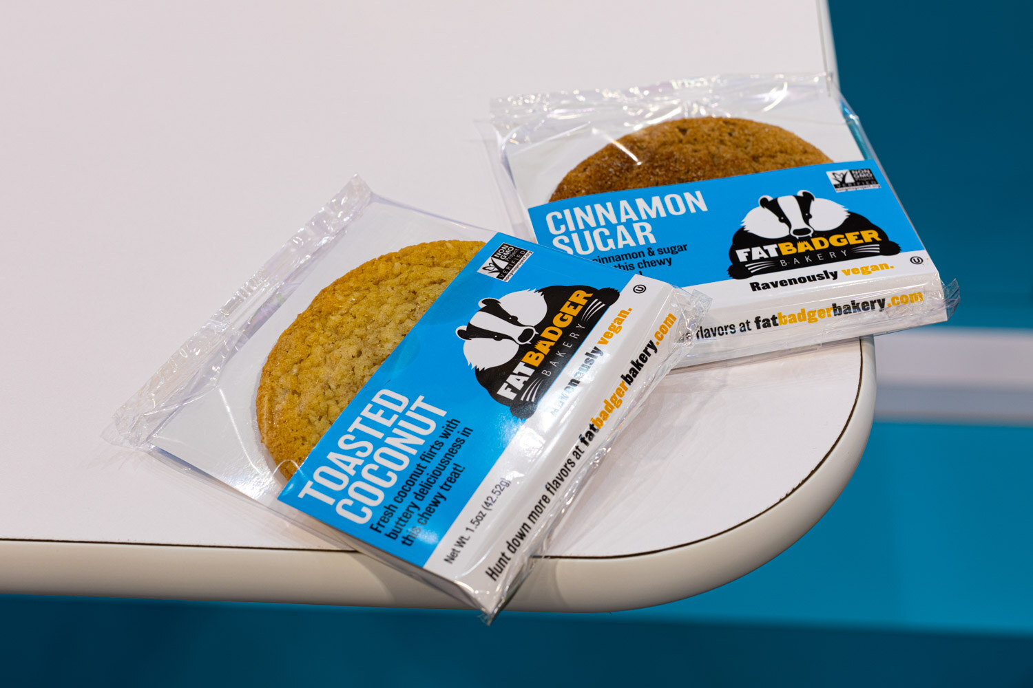 Two Fat Badger cookie packs, Toasted Coconut and Cinnamon Sugar, lie on a white table