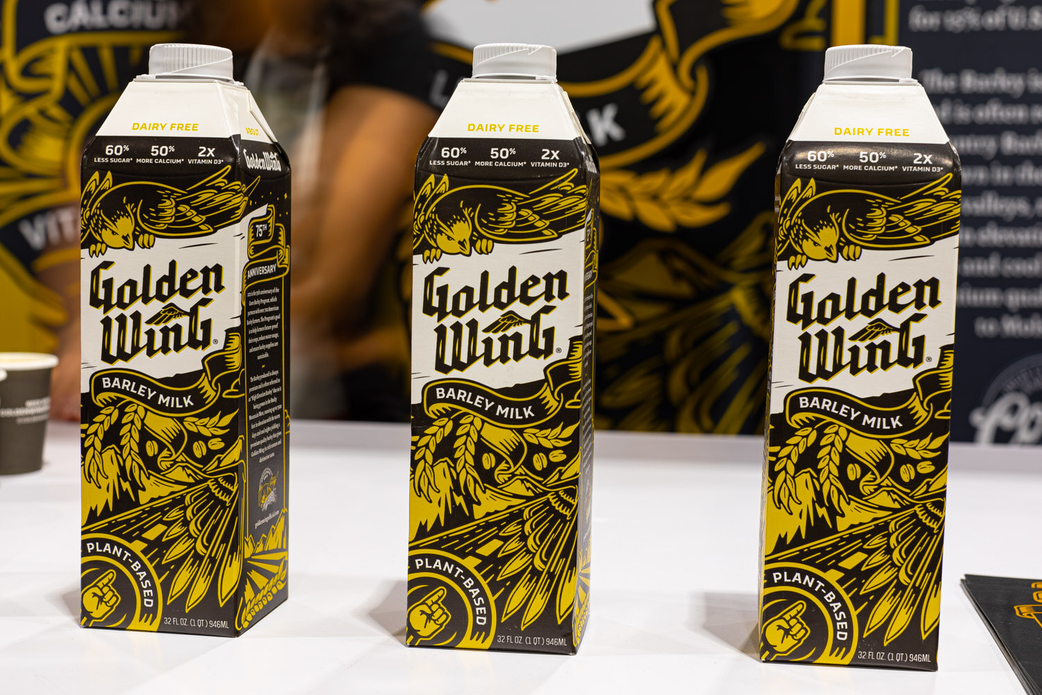 Three black and yellow Golden Wing barley milk cartons stand in a row on a white counter