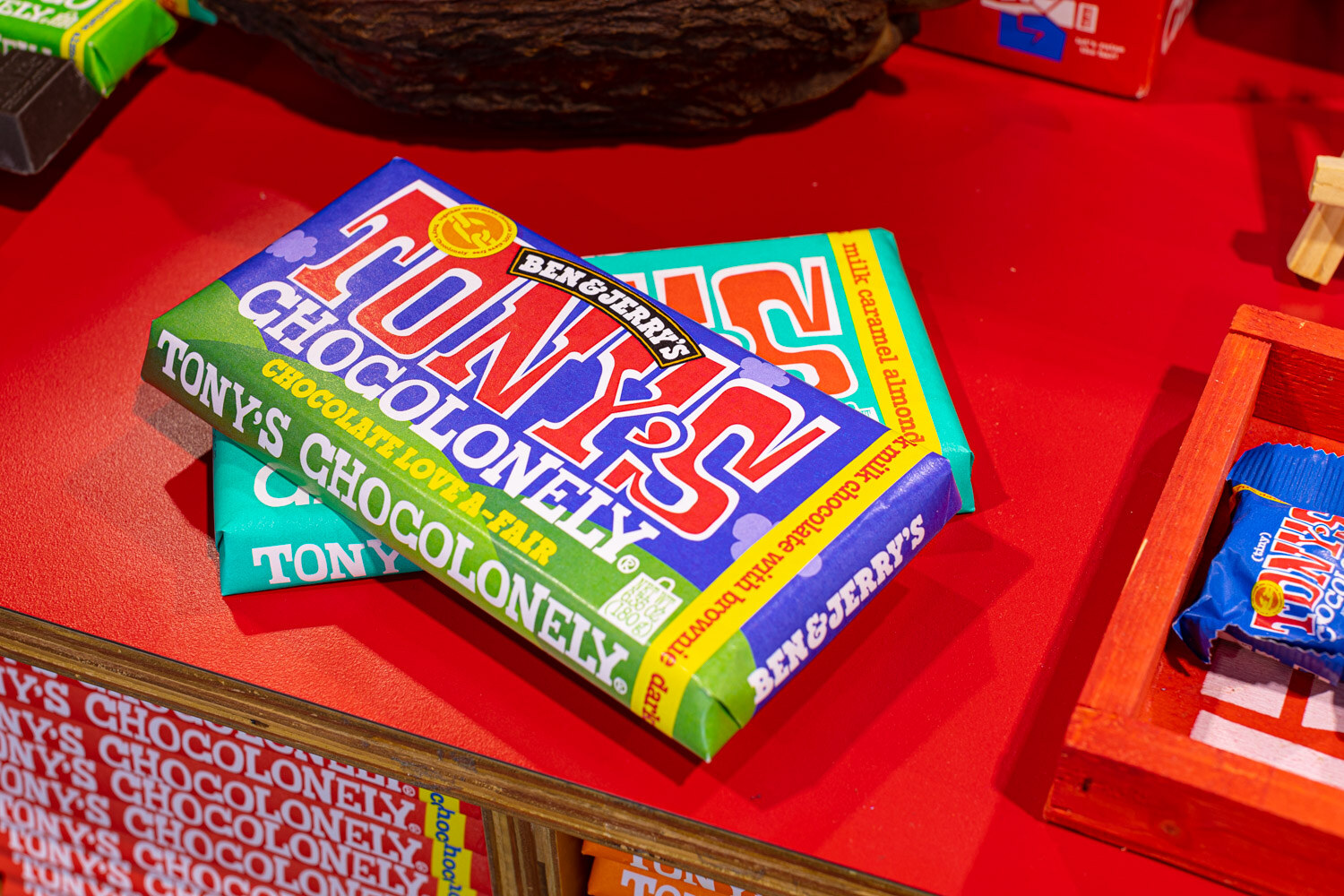 Colorful Tony's Chocolonely bars lie on a bright red table with a repeating pattern behind them