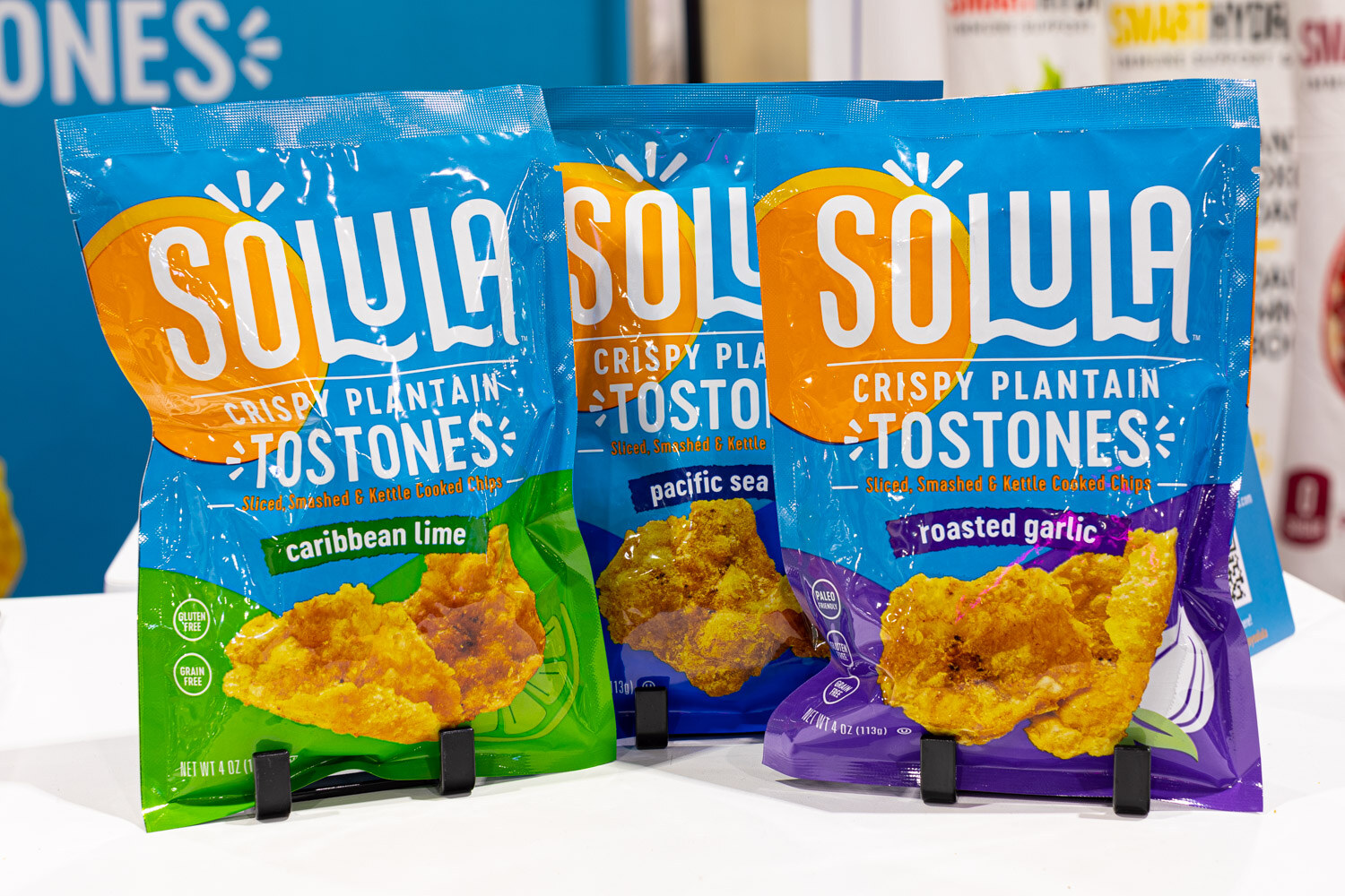 Three Solula crispy plantain tostones bags in caribbean lime, pacific sea salt and roasted garlic stand on small black easels