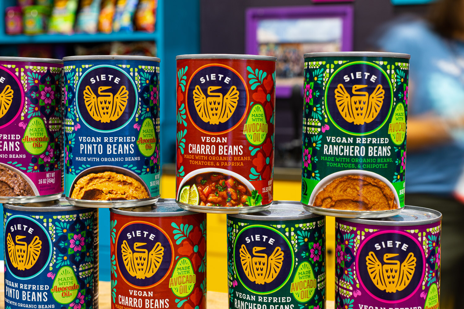 Stacked Siete vegan refried bean cans in pinto, charro and ranchero flavors with bright patterned labels