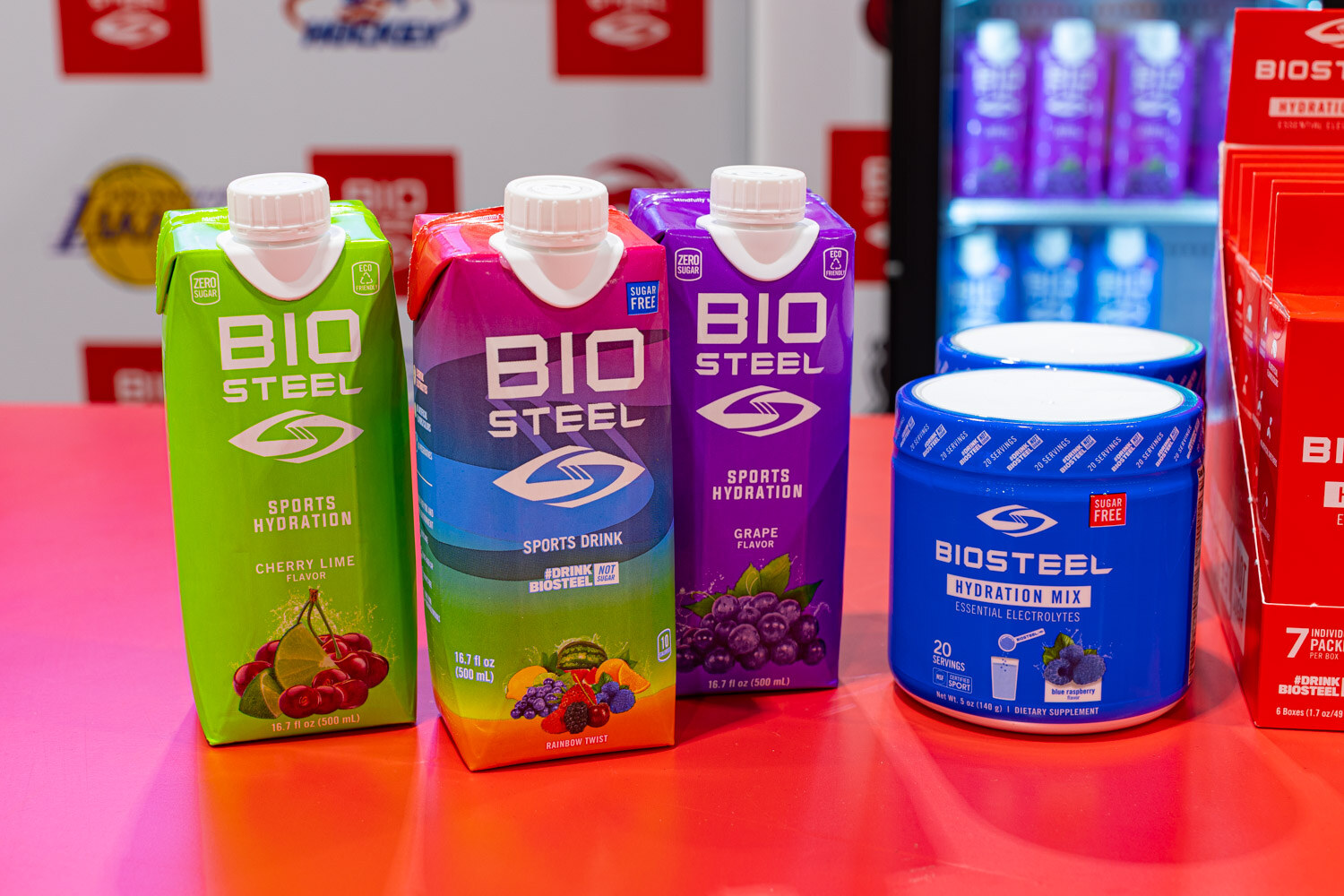 BioSteel cartons in cherry lime, blue raspberry and grape, plus a tub of hydration mix, sit on a pink and orange table