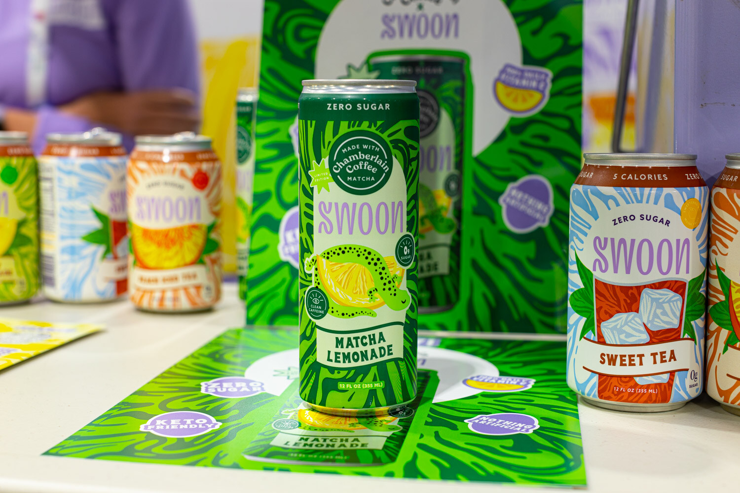 Swoon cans in matcha lemonade and sweet tea flavors stand on a green patterned table