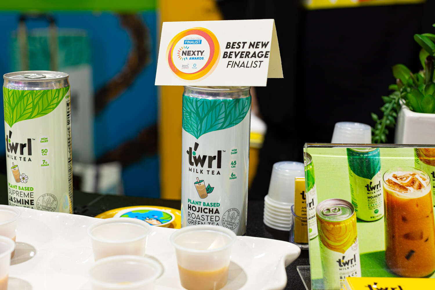 twrl Hojicha and Jasmine milk tea cans stand next to sample cups and a Nexty Awards Best New Beverage finalist sign