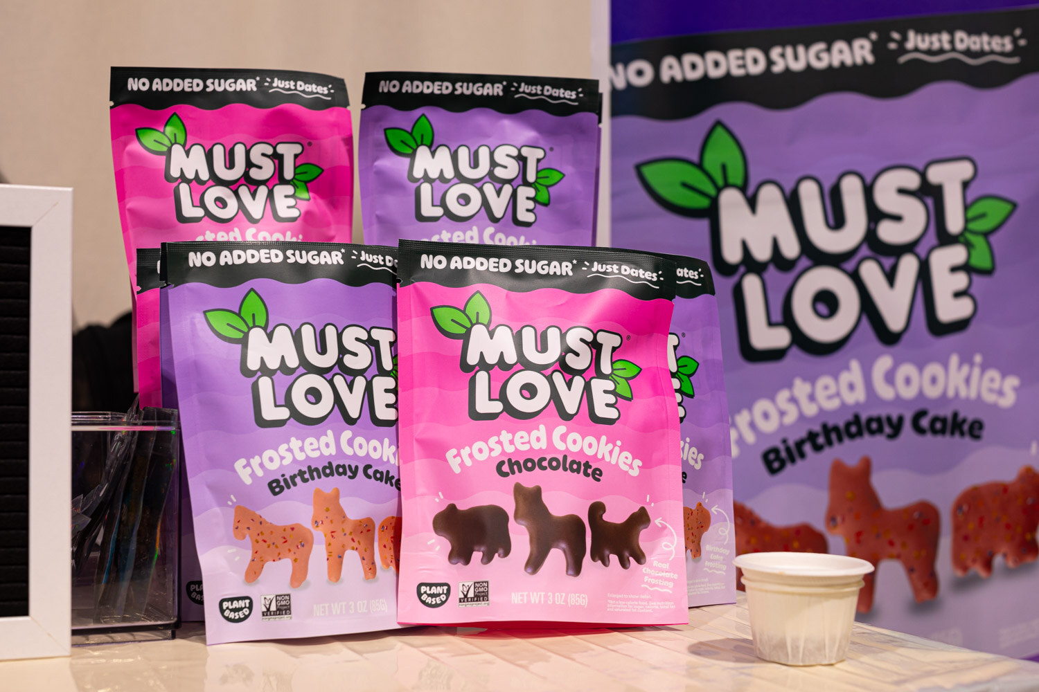 Purple Must Love Frosted Cookies bags in Birthday Cake and Chocolate stand beside a large Must Love bag
