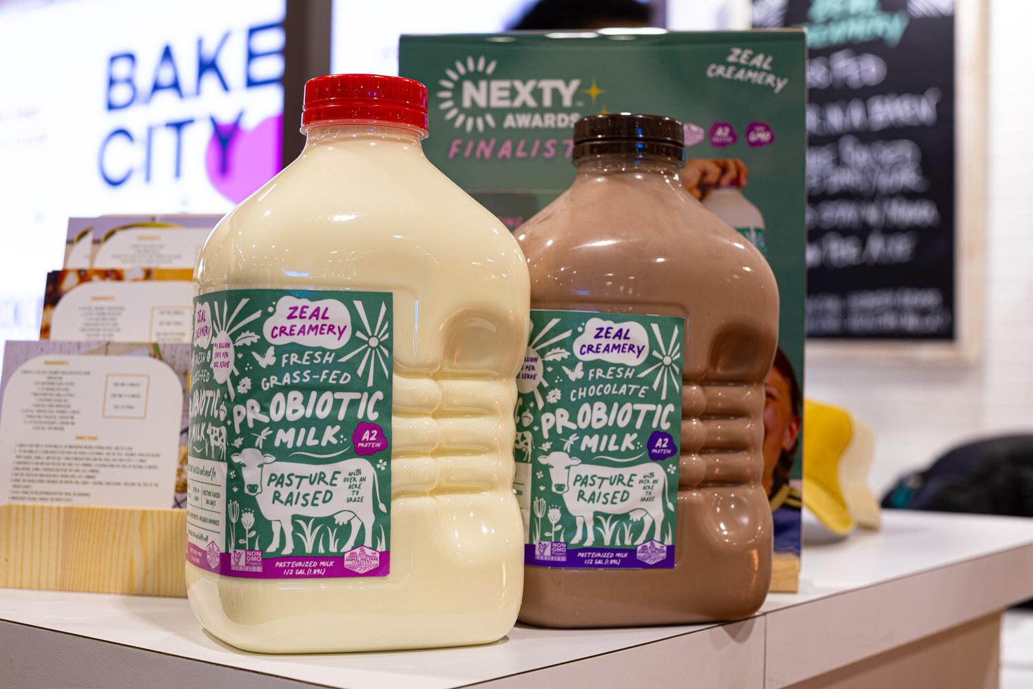 Jugs of Zeal Creamery fresh grass-fed probiotic milk in plain and chocolate stand beside a Nexty Awards finalist sign
