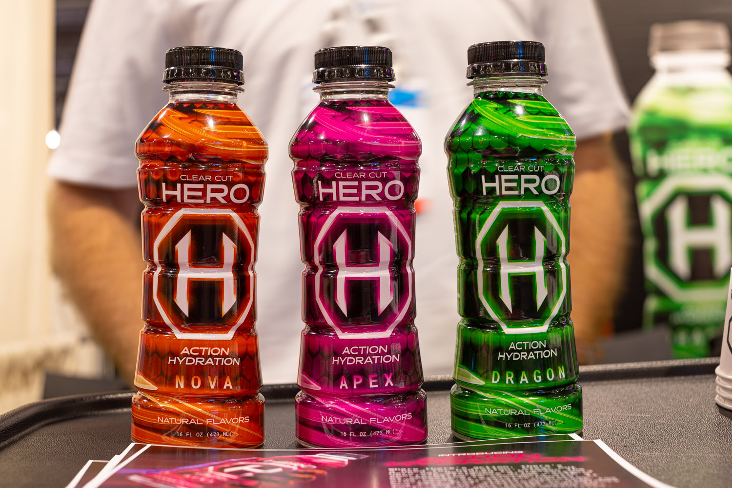 Three Hero Action Hydration bottles named Nova, Apex and Dragon in orange, pink and green stand in a row