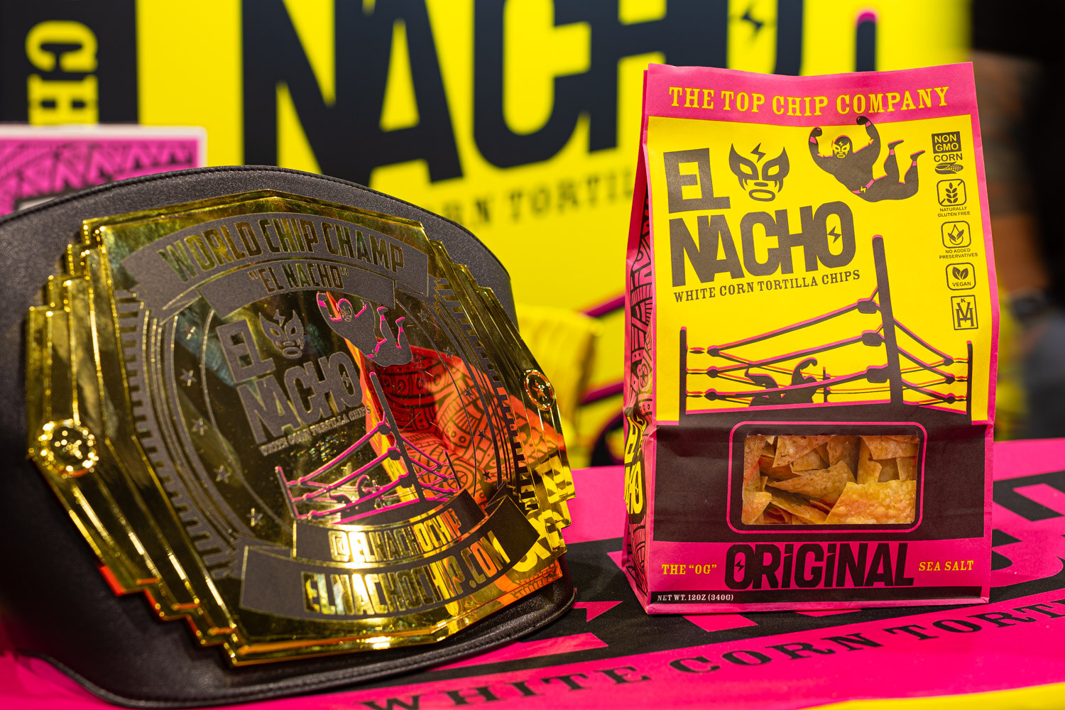 A gold championship-style belt sits beside a yellow El Nacho white corn tortilla chip bag