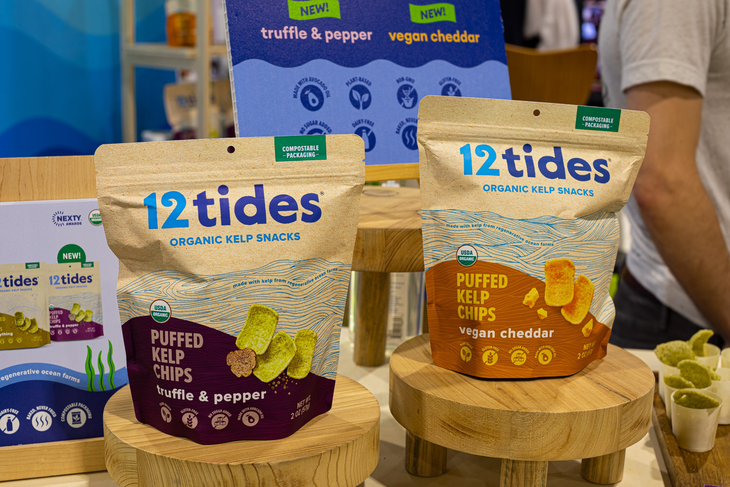 Two 12 tides puffed kelp chip bags in truffle and pepper and vegan cheddar flavors stand on small wooden risers