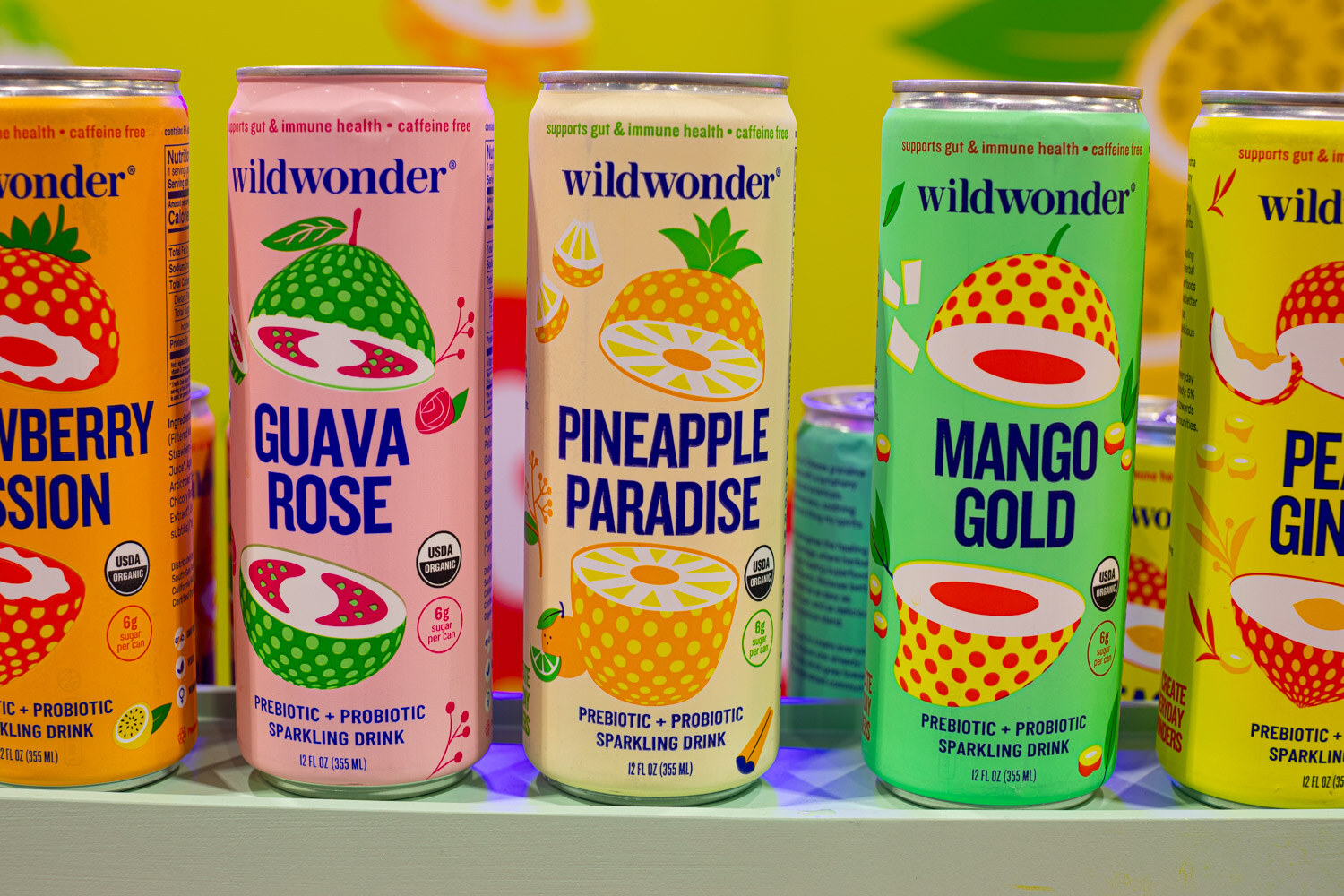Wildwonder cans in guava rose, pineapple paradise and mango gold flavors stand on a lit shelf