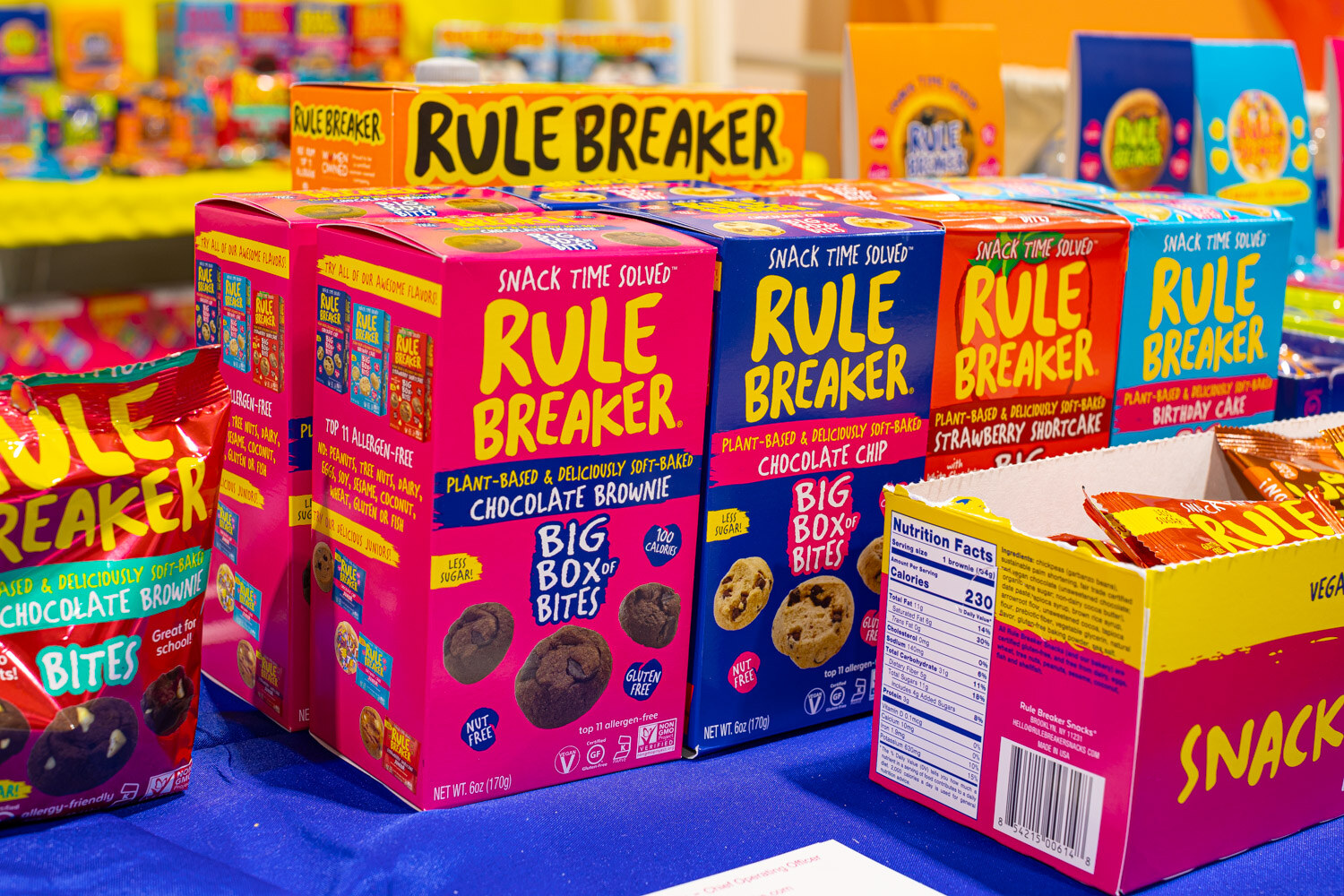 Pink and blue boxes of Rule Breaker Big Box Bites in chocolate brownie and strawberry shortcake stand on a table with other boxes