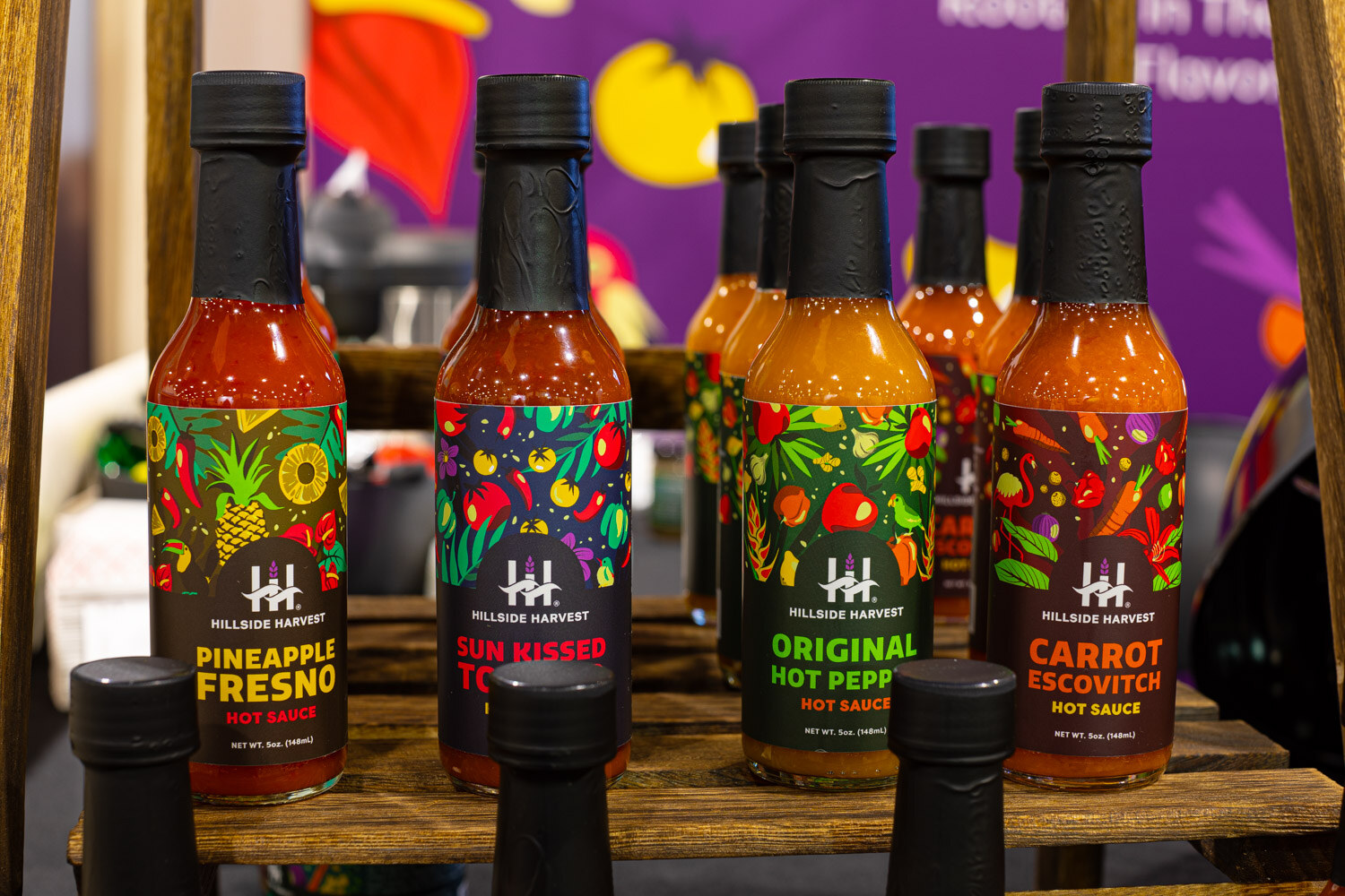 Bottles of Hillside Harvest hot sauce in Pineapple Fresno, Sun Kissed Tomato, Original Hot Pepper and Carrot Escovitch flavors against a purple backdrop