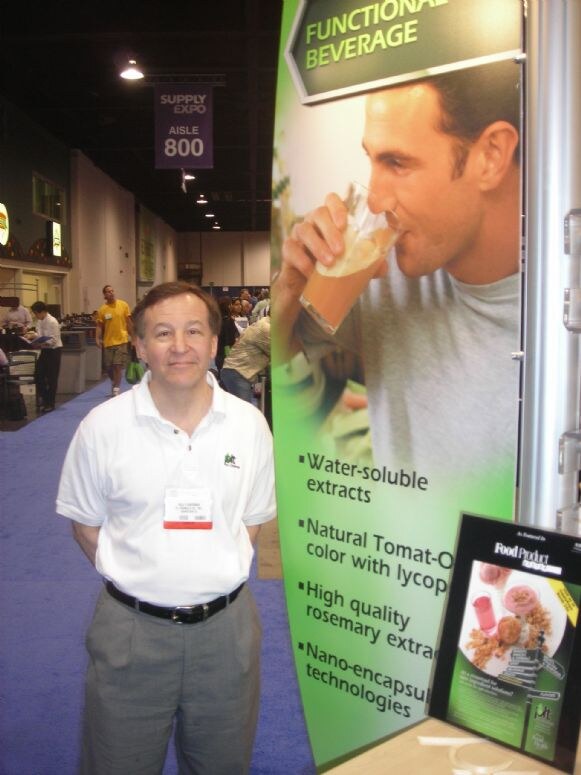 A man in a white polo stands beside a green Functional Beverage banner listing extracts and nano-encapsulation, with a Food Product Design magazine ad nearby in the Supply Expo aisle.
