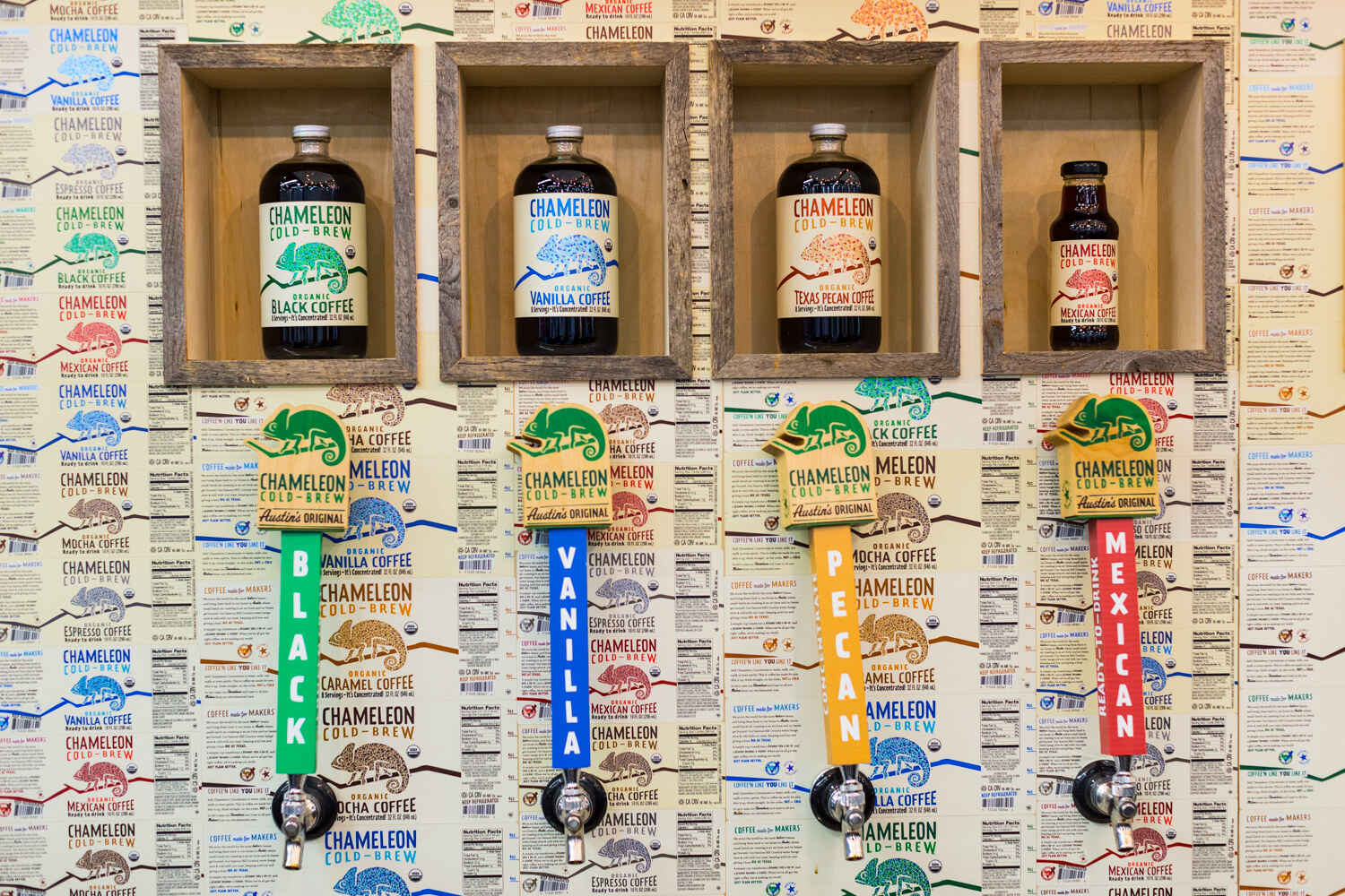 Wall of Chameleon Cold-Brew labels with four wooden boxes holding bottles above taps marked Black, Vanilla, Pecan and Mexican.
