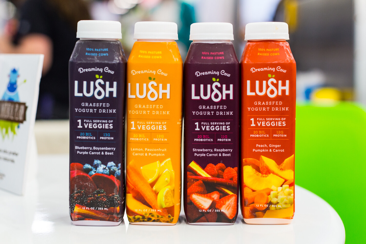 Four Lush by Dreaming Cow grassfed yogurt drink bottles in blue, yellow, burgundy and orange flavors.