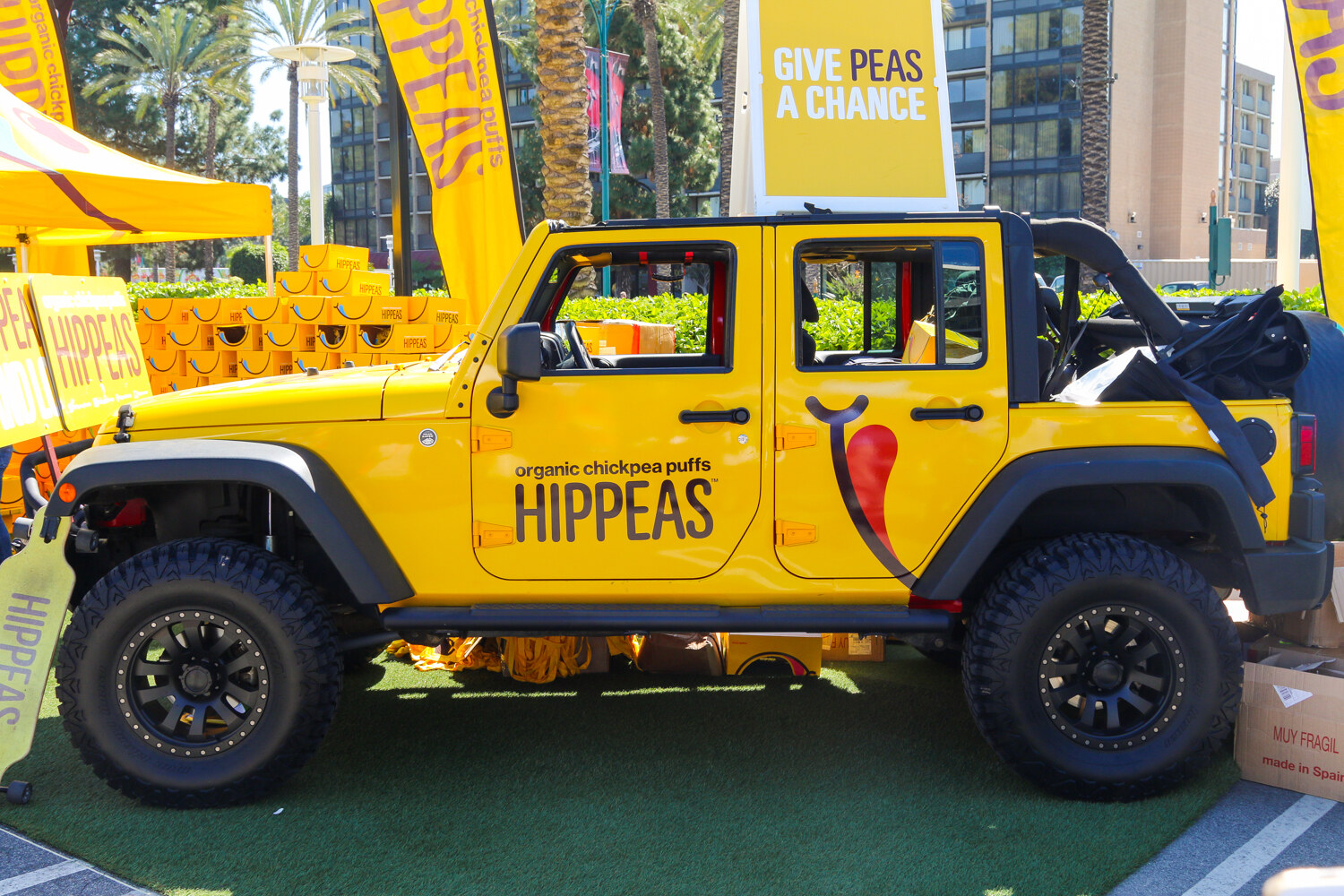 Yellow jeep labeled Hippeas organic chickpea puffs with a Give Peas a Chance sign and stacked yellow boxes behind it.