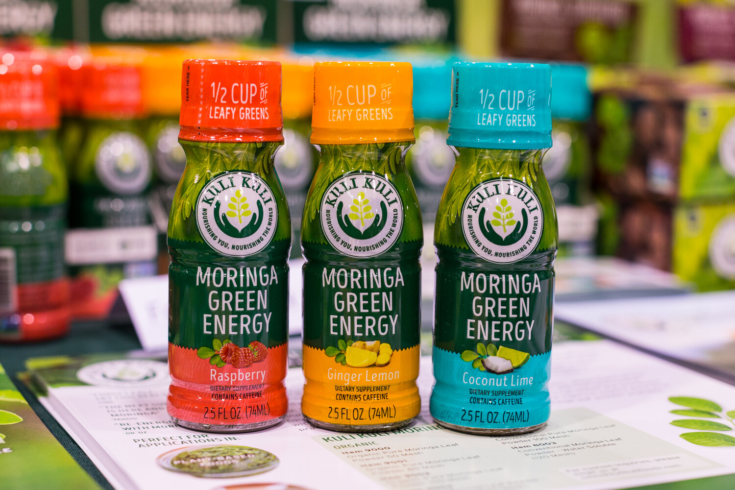 Three green Kuli Kuli Moringa Green Energy bottles with raspberry, ginger lemon and coconut lime labels.