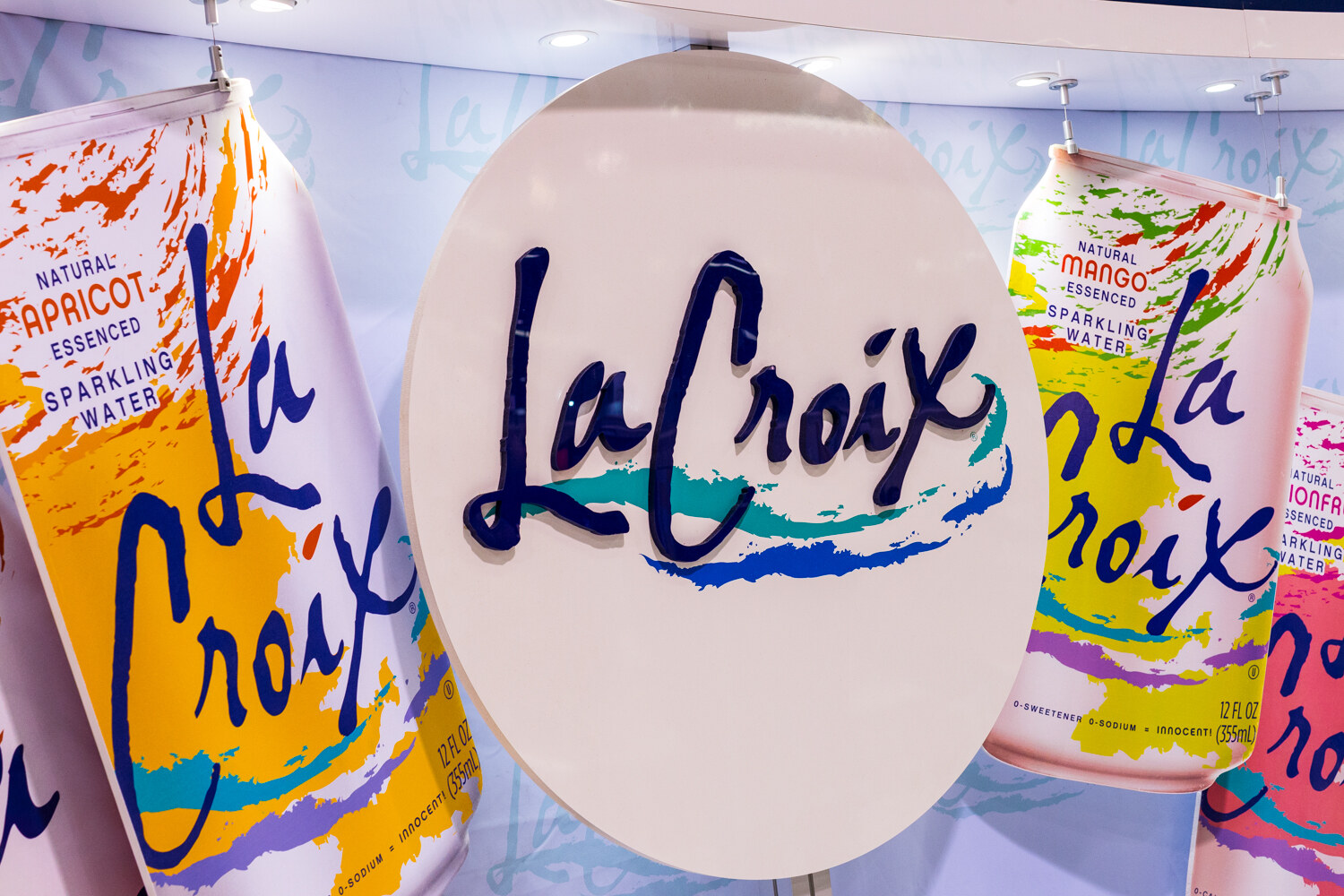 Round white La Croix sign flanked by oversized apricot and mango La Croix can graphics.