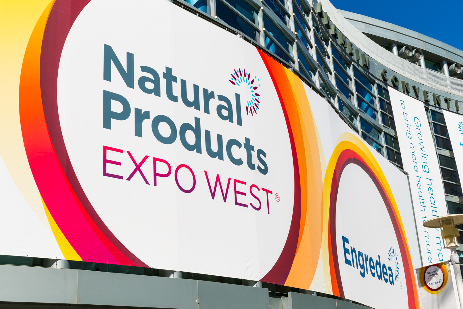 Large Natural Products Expo West banner with Engredea logo on the curved glass facade of the convention center under a blue sky.