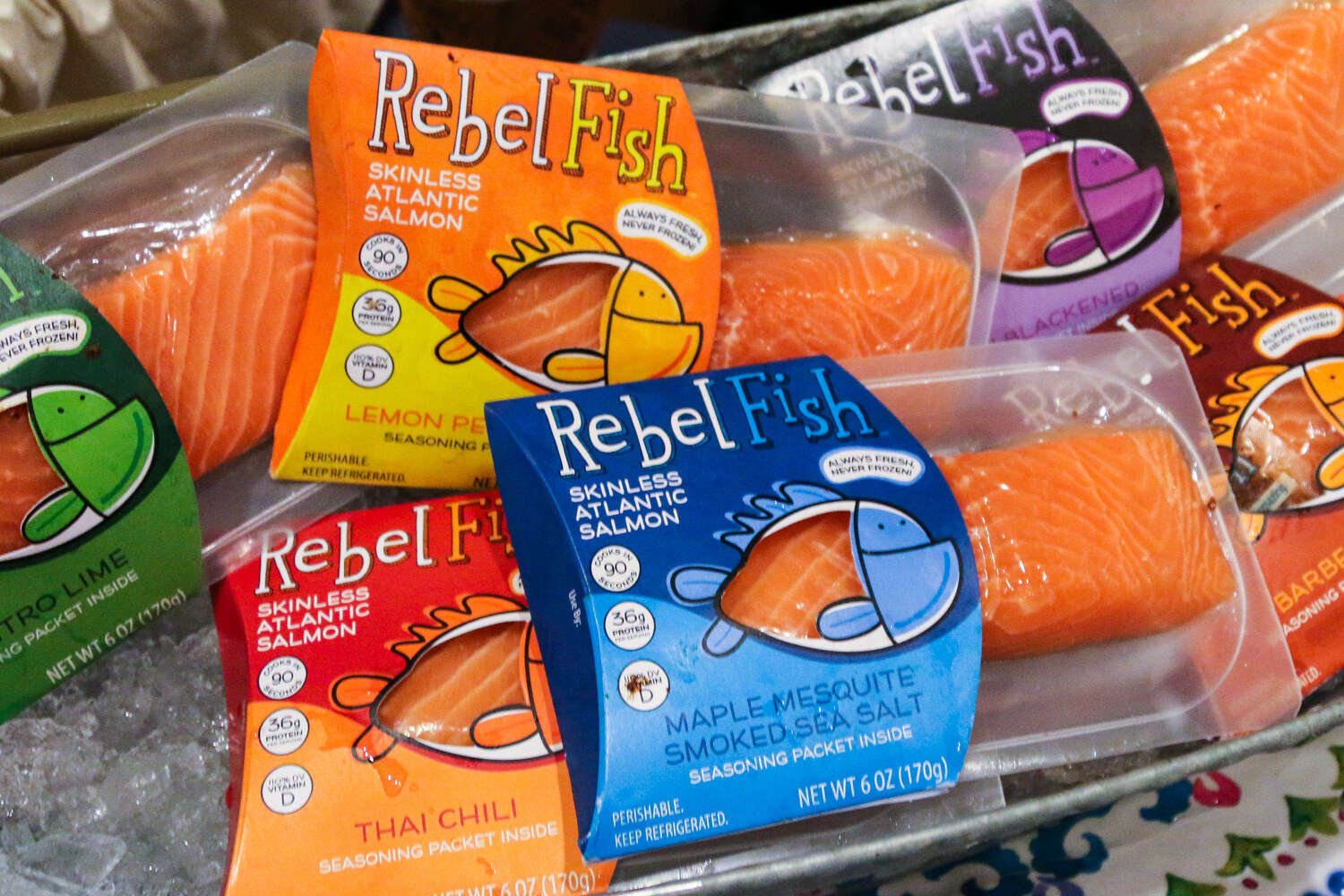 Colorful Rebel Fish salmon packages in lemon pepper, maple mesquite, Thai chili and other flavors lying on crushed ice.