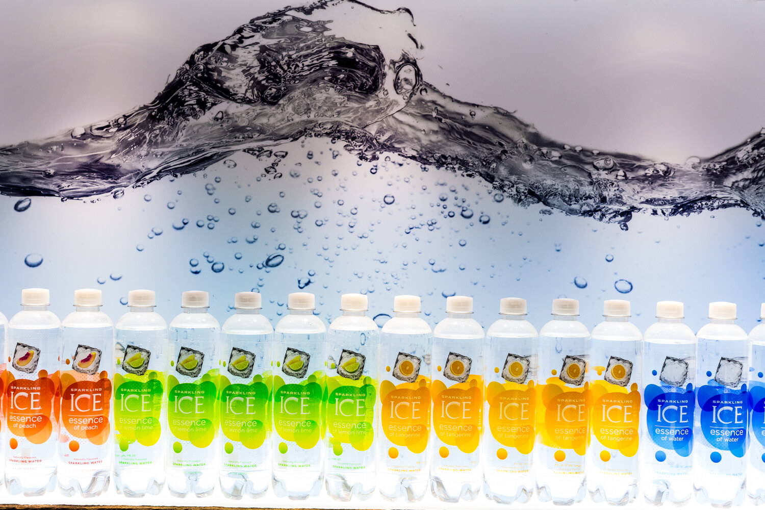 Row of Sparkling Ice bottles in peach, lemon lime, tangerine and water flavors beneath a photo of a water wave.