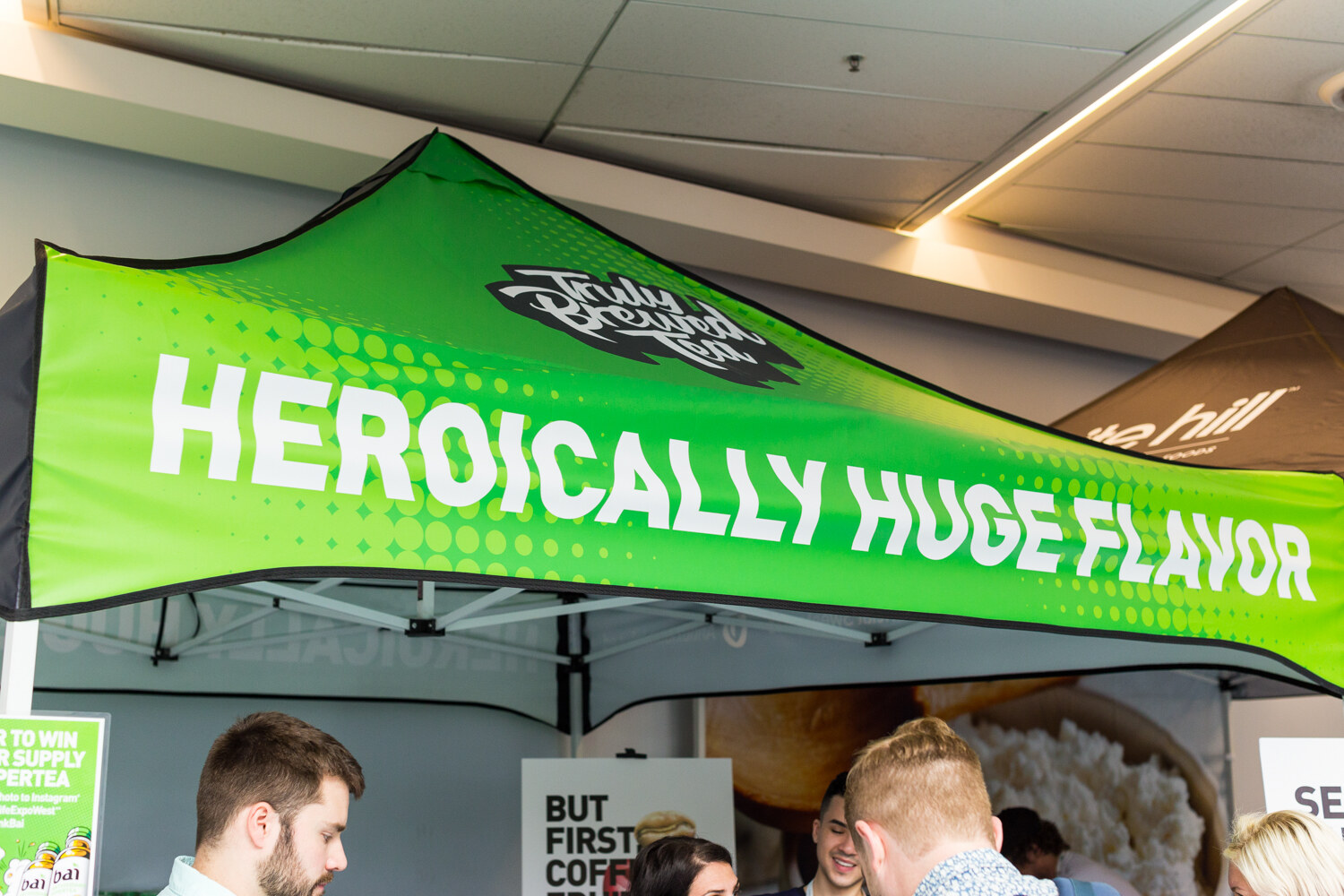 Green pop-up tent printed Heroically Huge Flavor with a Truly Brewed Tea logo and several attendees beneath it.