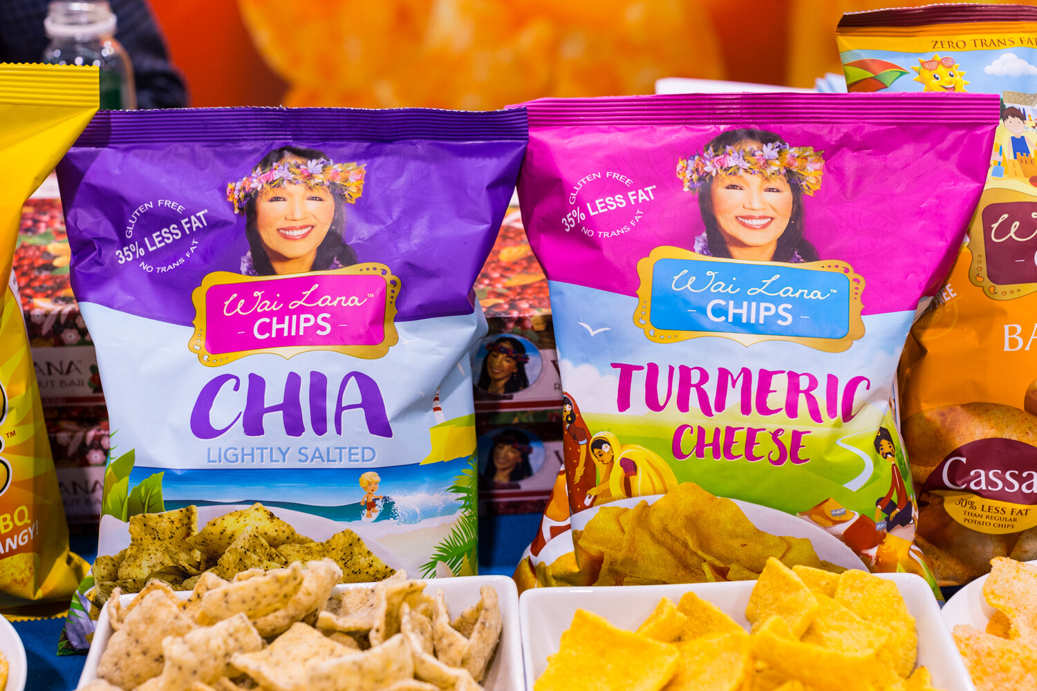 Bags of Wai Lana Chips in Chia and Turmeric Cheese flavors in front of bowls of chips.